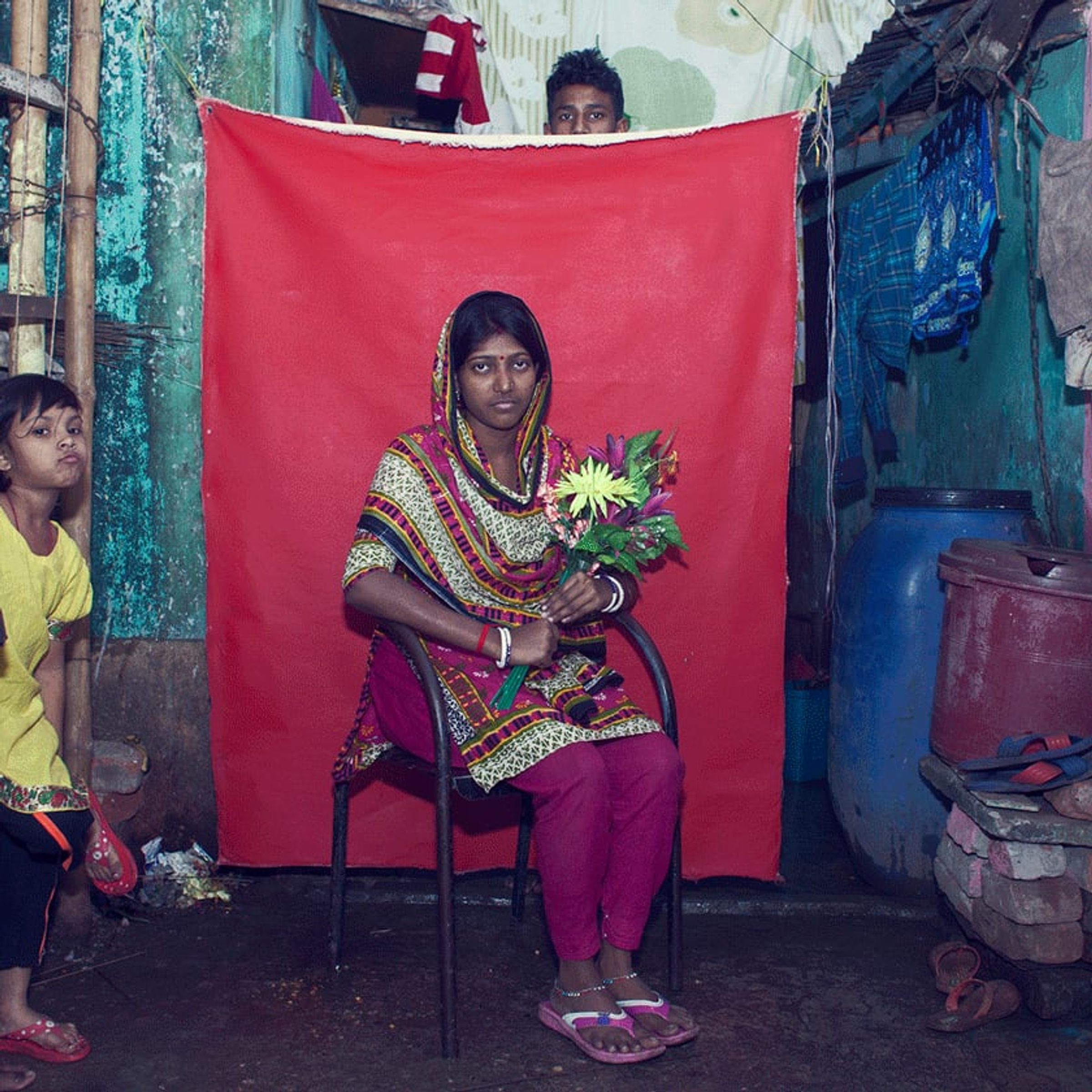 Seated person holds green leaves and flowers while a child peeks from the edge.