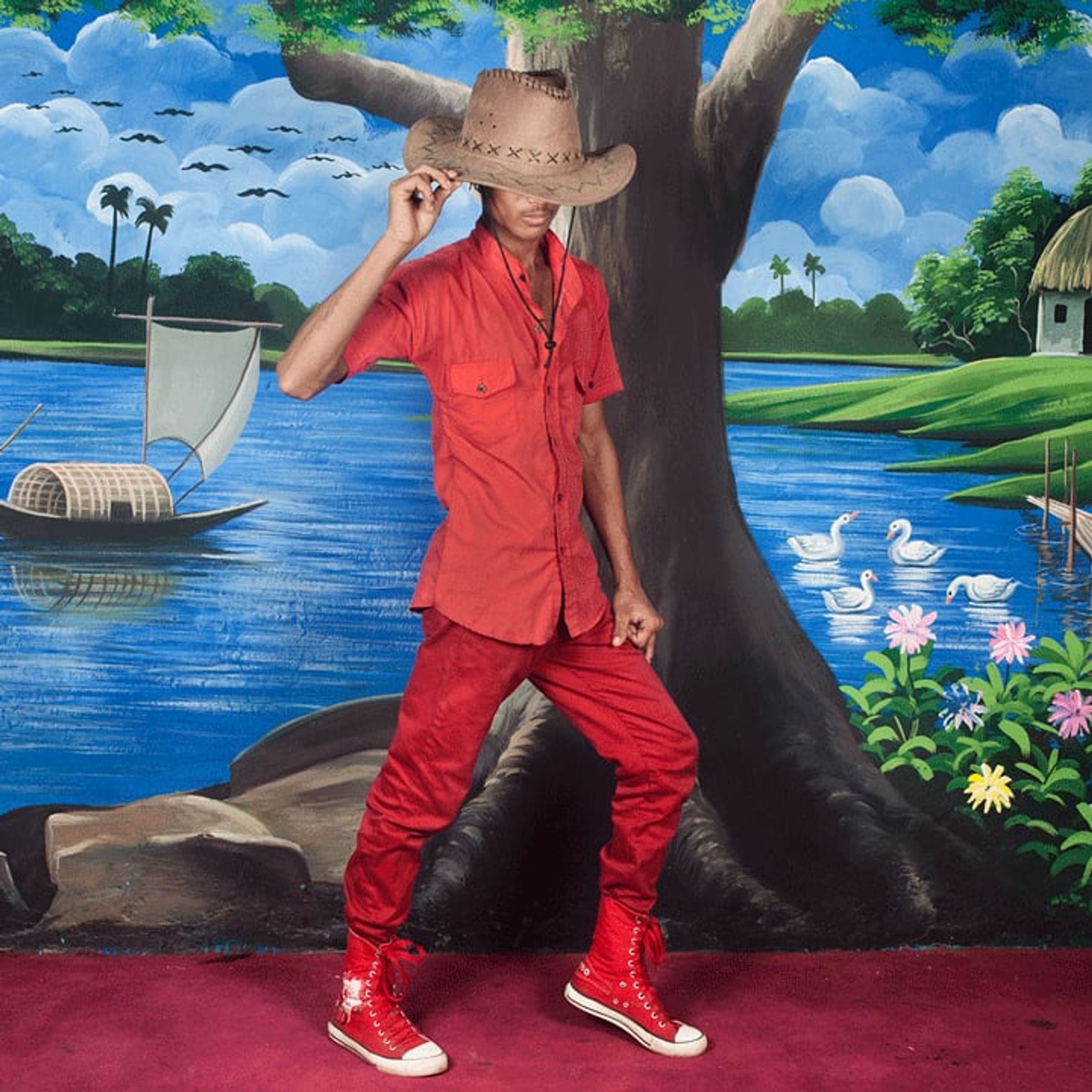 Person in red clothing and a cowboy hat shades their face before a painted river.