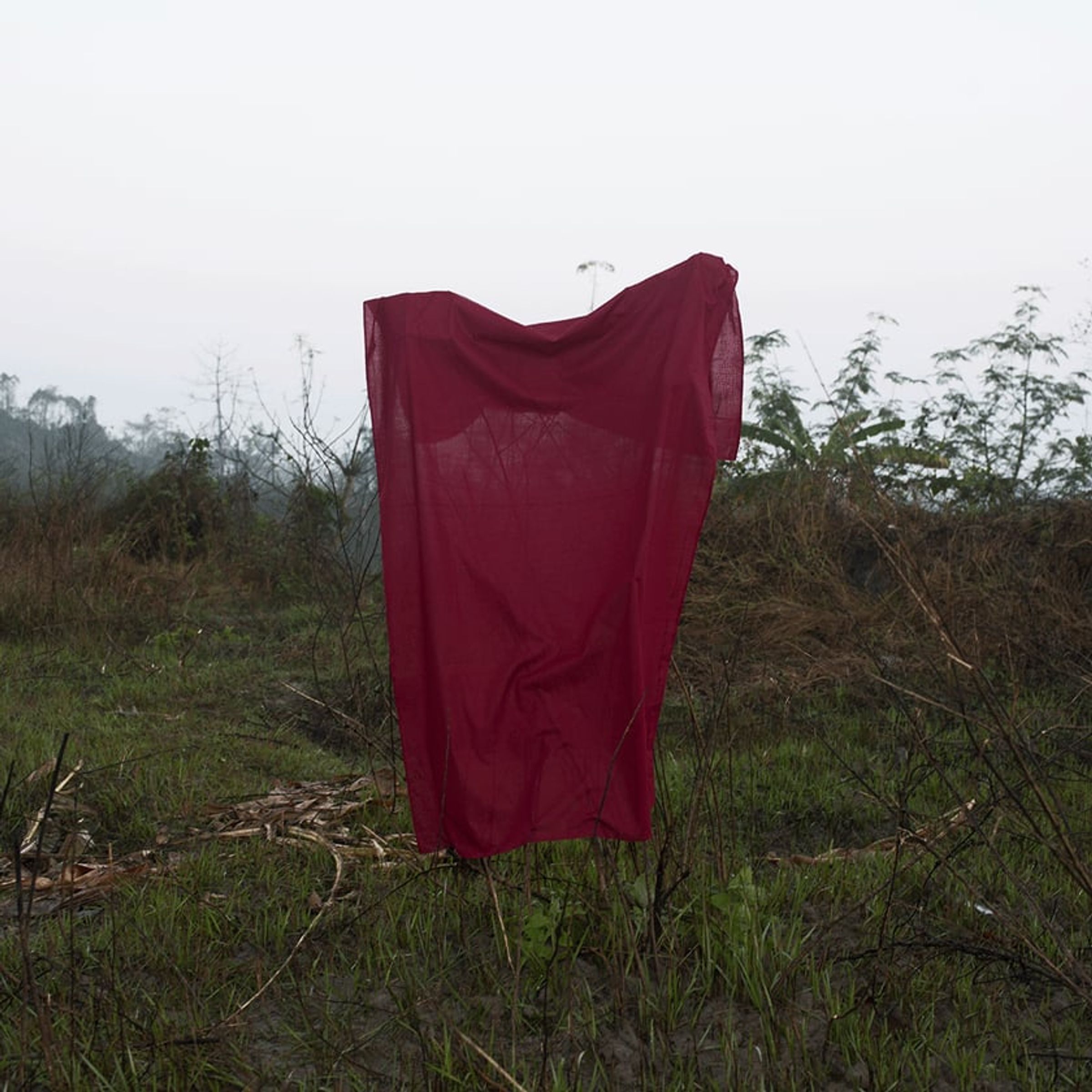 Red cloth drapes over a simple frame in a sparse green clearing.