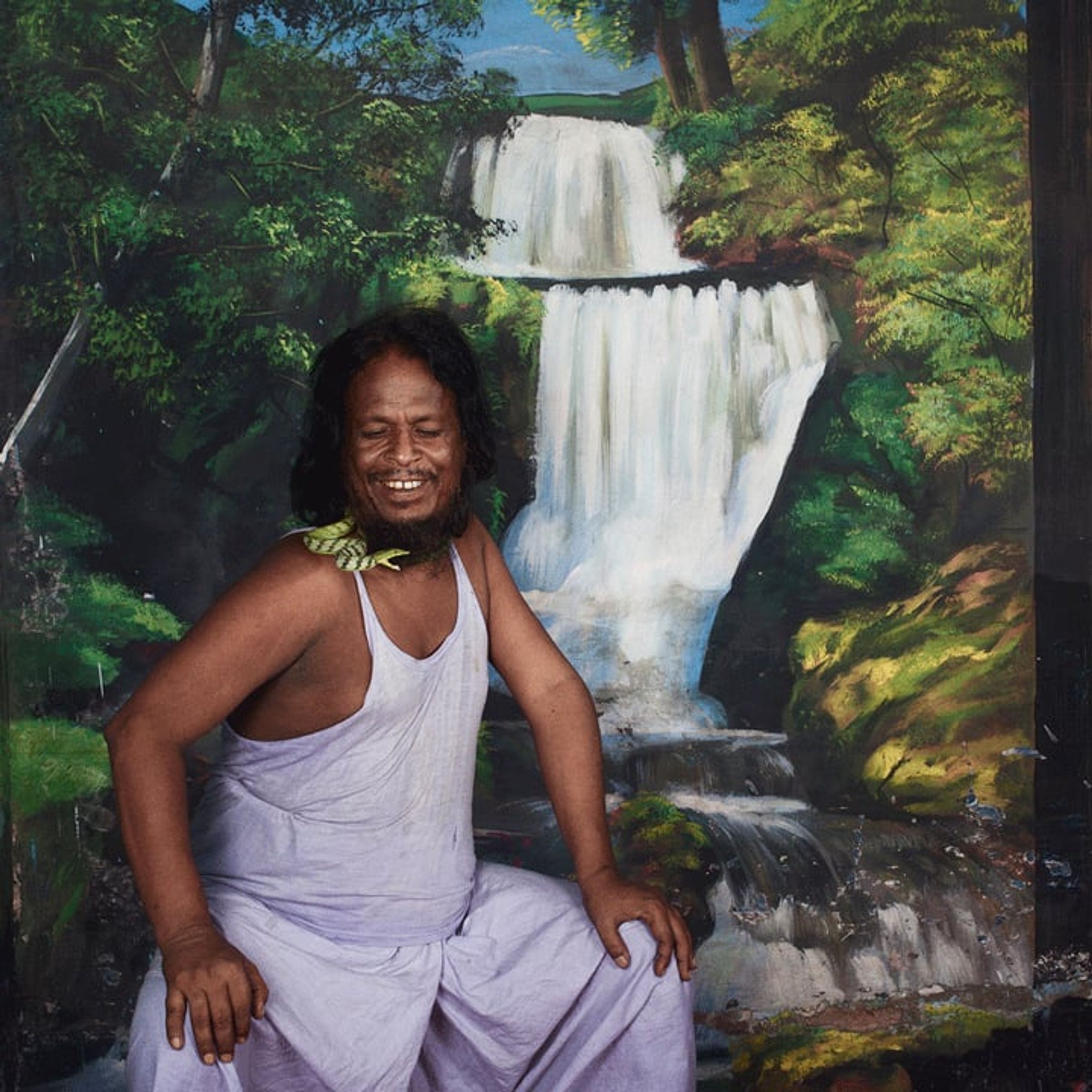 Seated person smiles before a painted waterfall and forest scene.
