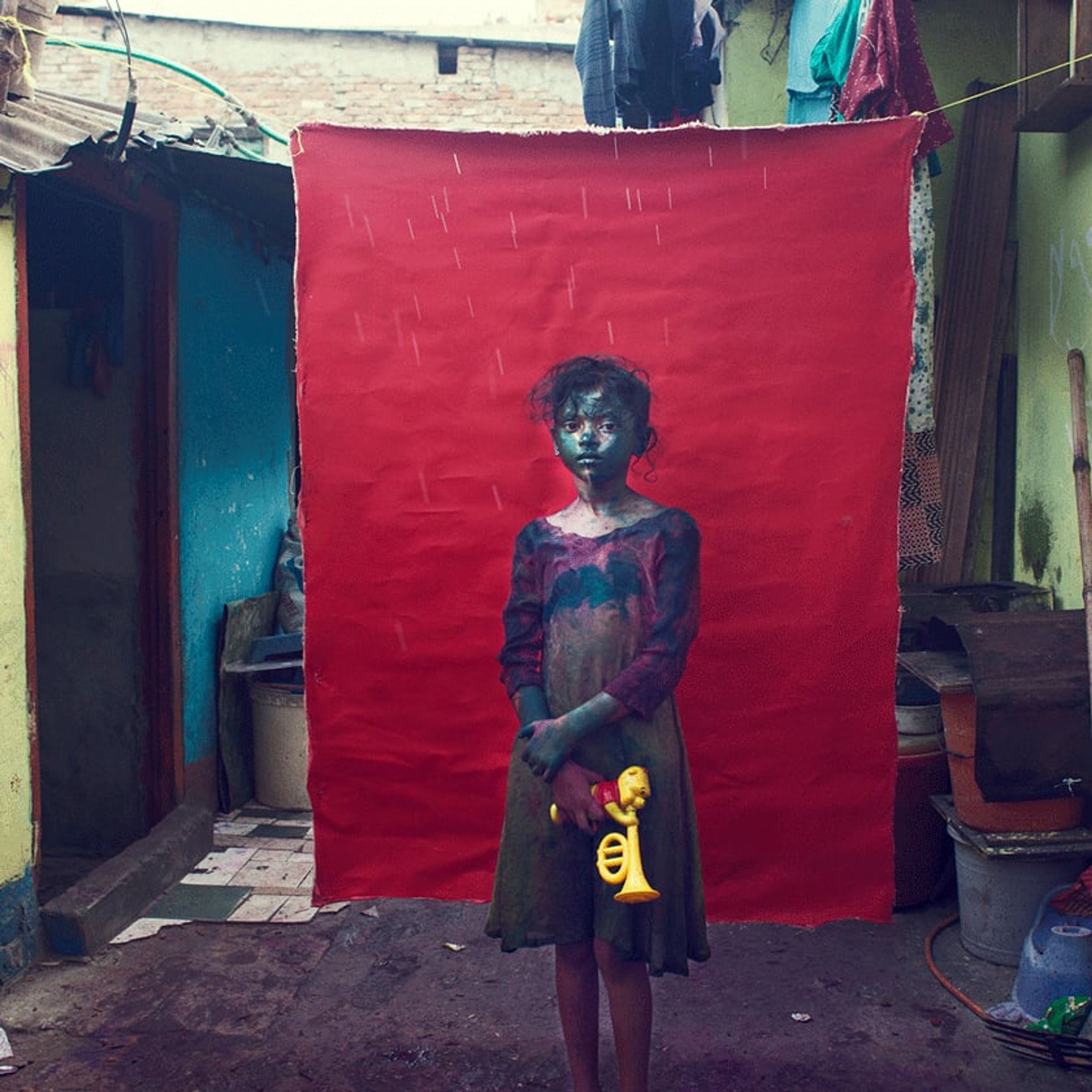 Young person in a dark dress holds a bright yellow object before a red cloth backdrop.