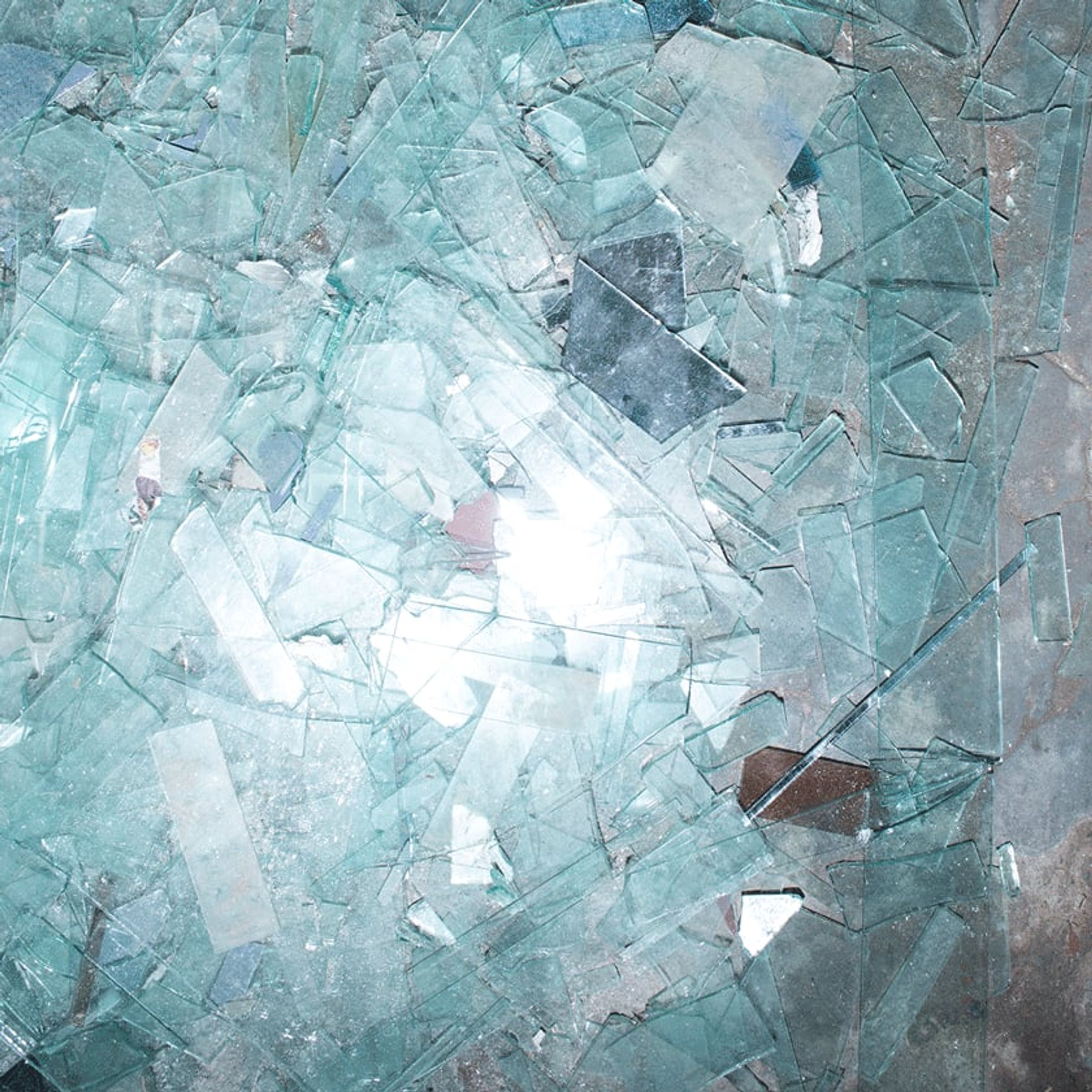 Broken glass shards overlap in a dense field of pale blue reflections.
