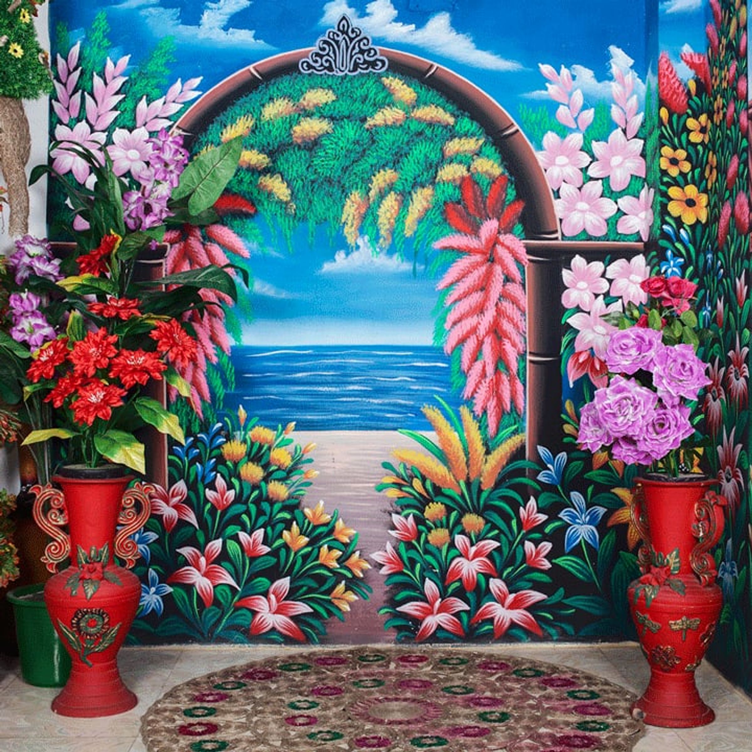 Toddler sits before a brightly painted garden backdrop with a red car.