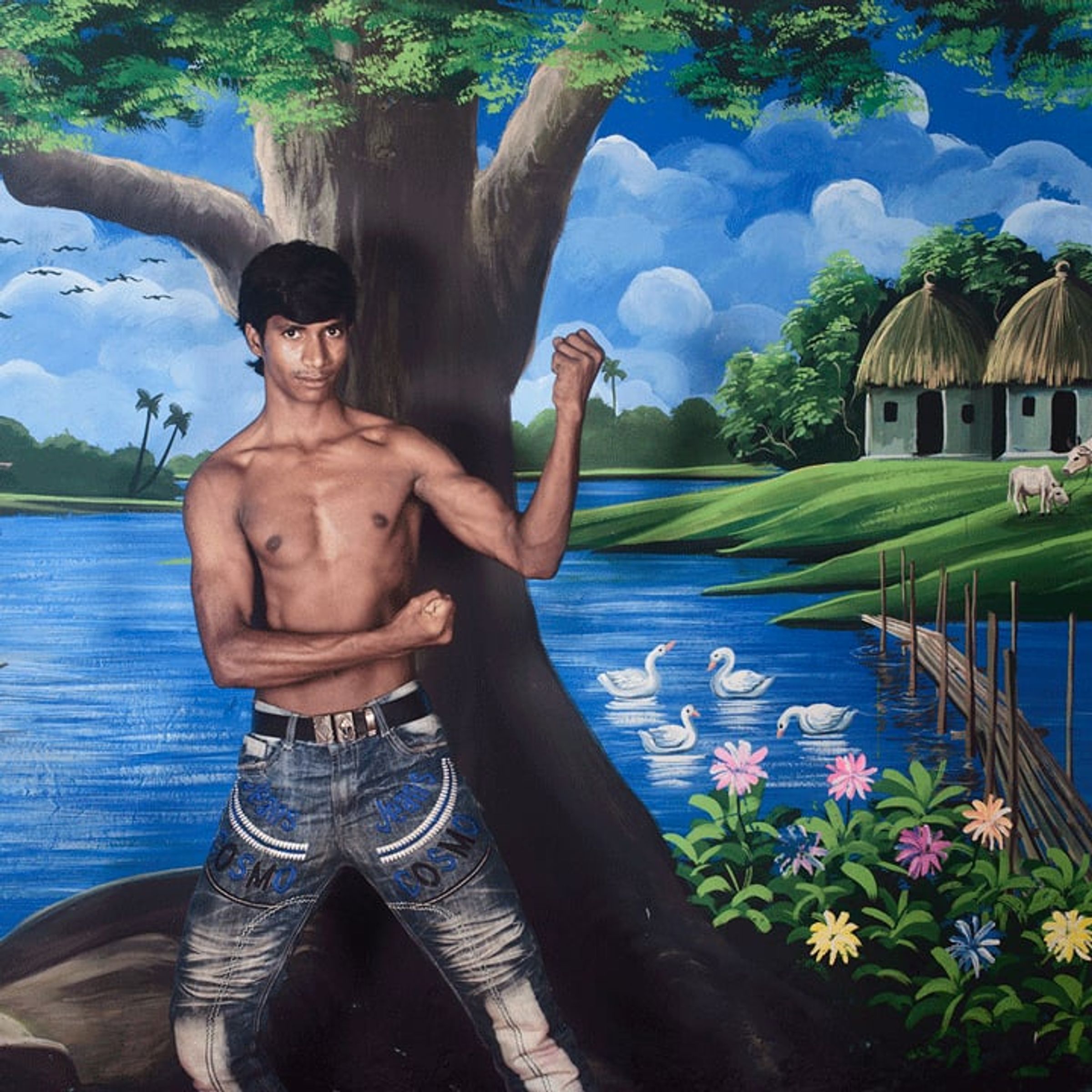 Shirtless man flexes one arm before a painted lakeside tree and boat.