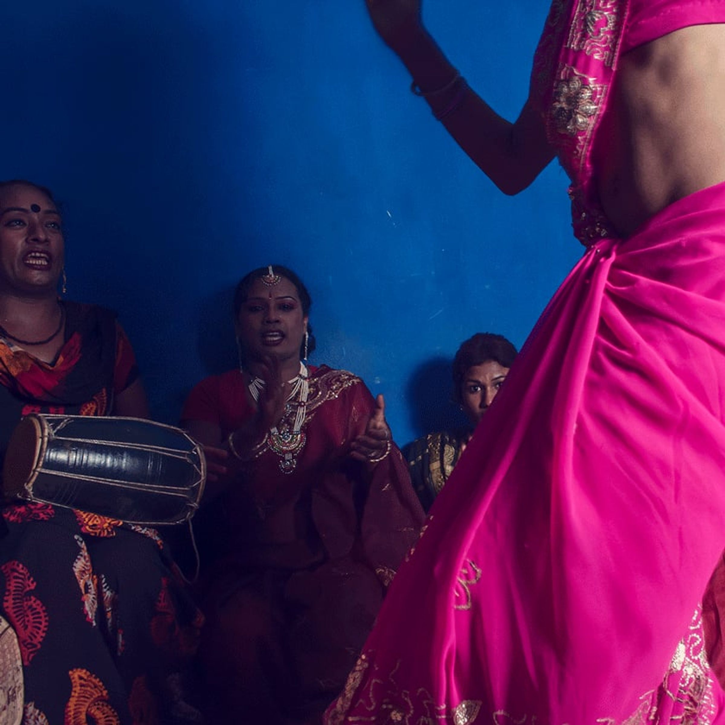 Bright pink fabric sweeps across the foreground while seated musicians and onlookers perform behind.