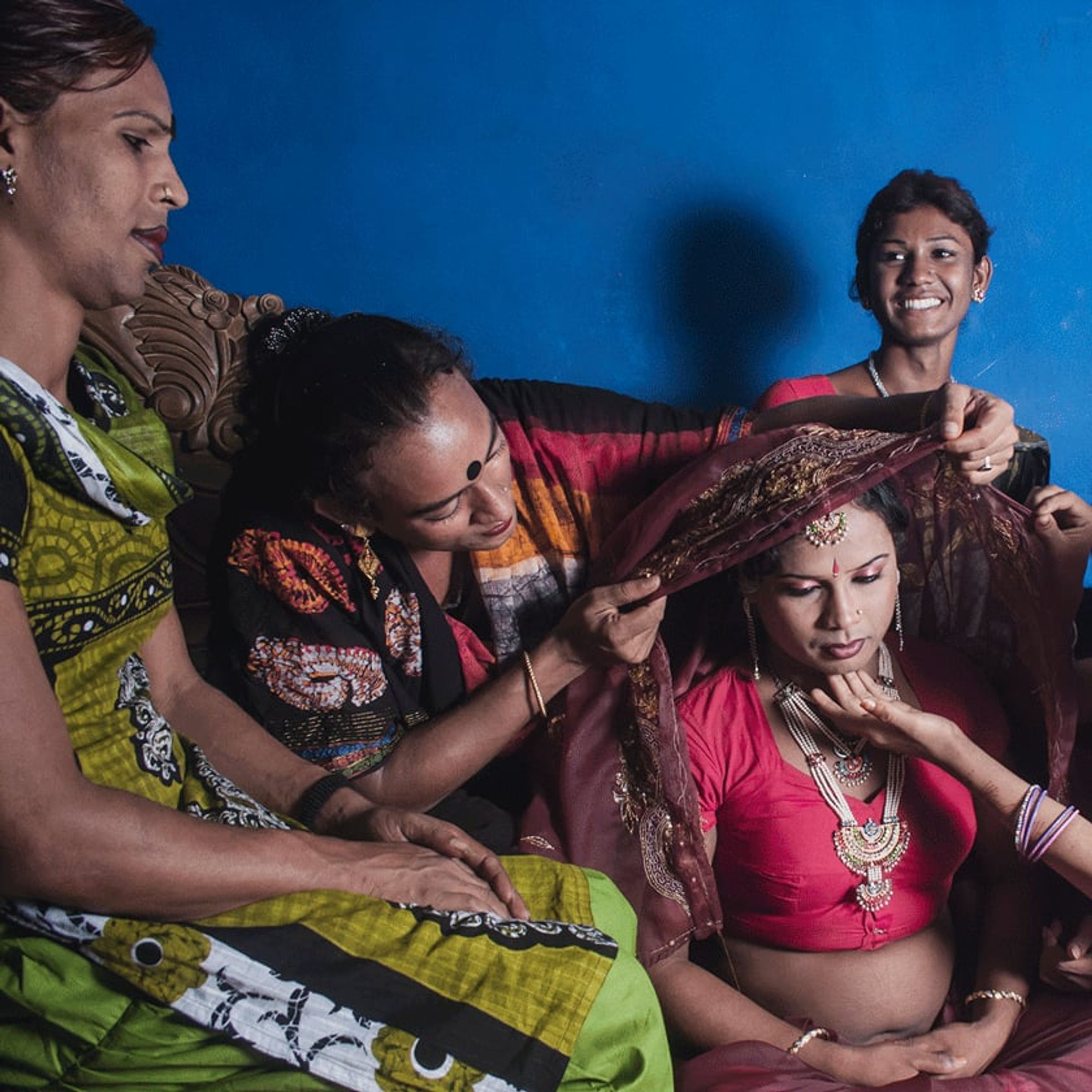Several people apply makeup and jewelry to a seated person in bright pink.