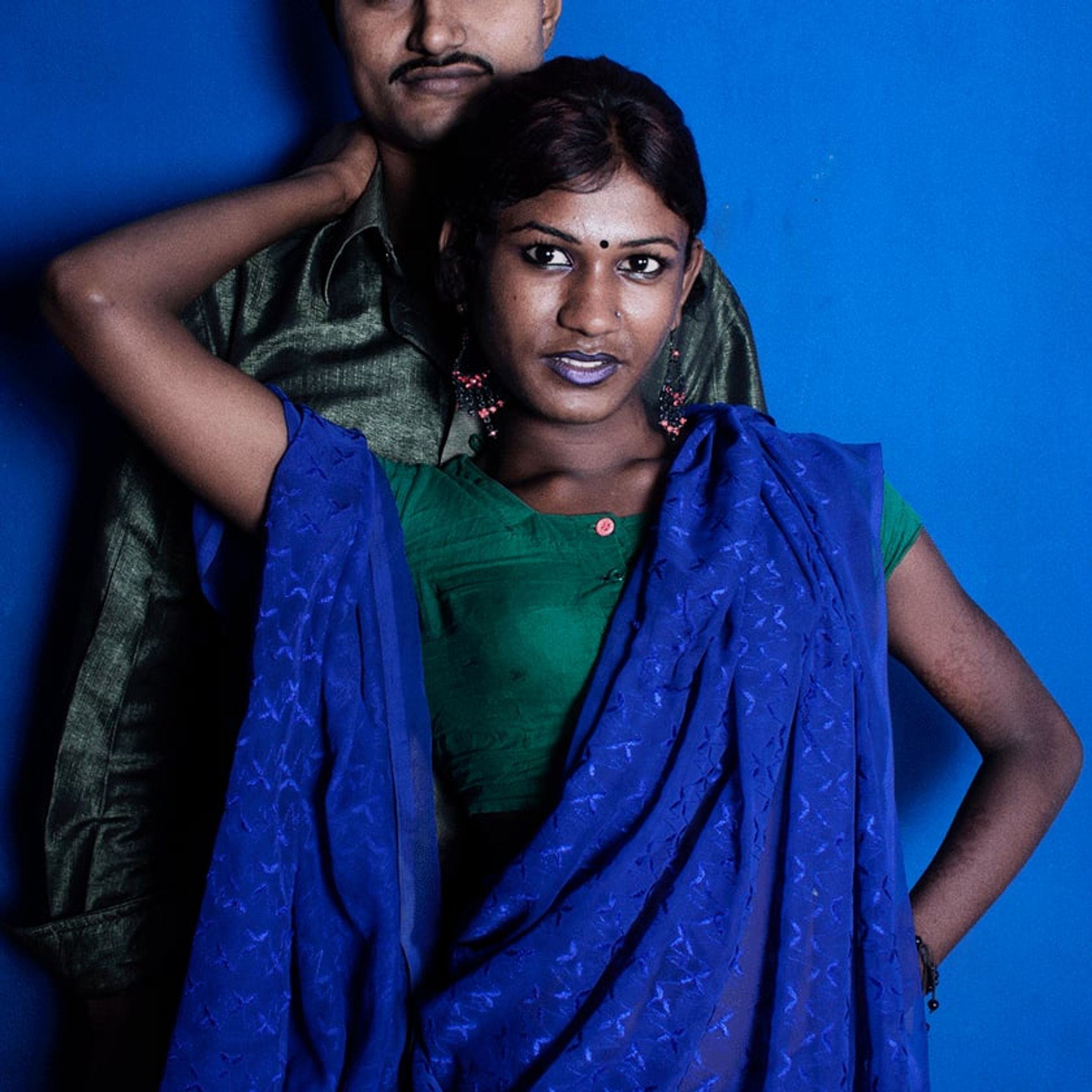 Person in blue and green drapery poses with one arm raised behind their head.
