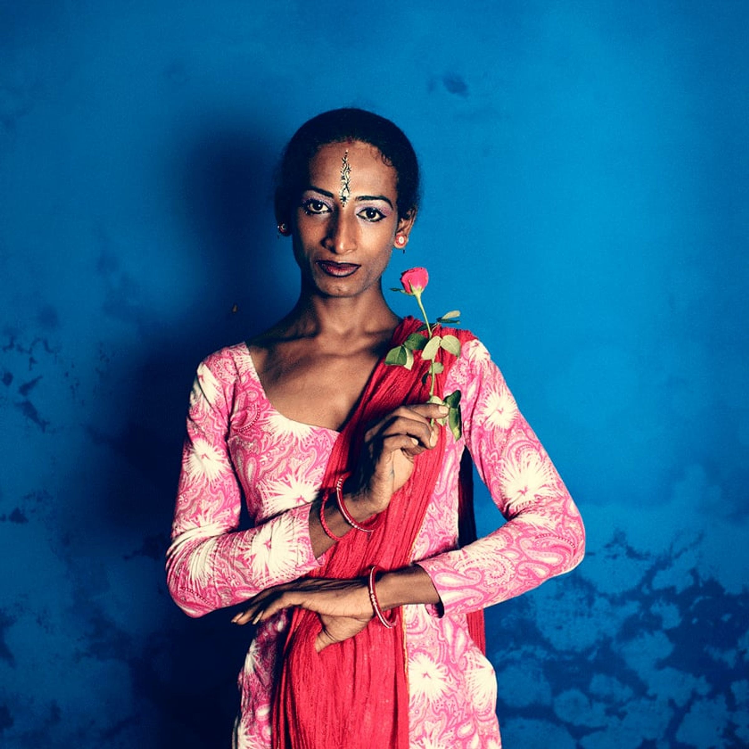 Person in bright pink holds a red rose and looks directly toward the camera.