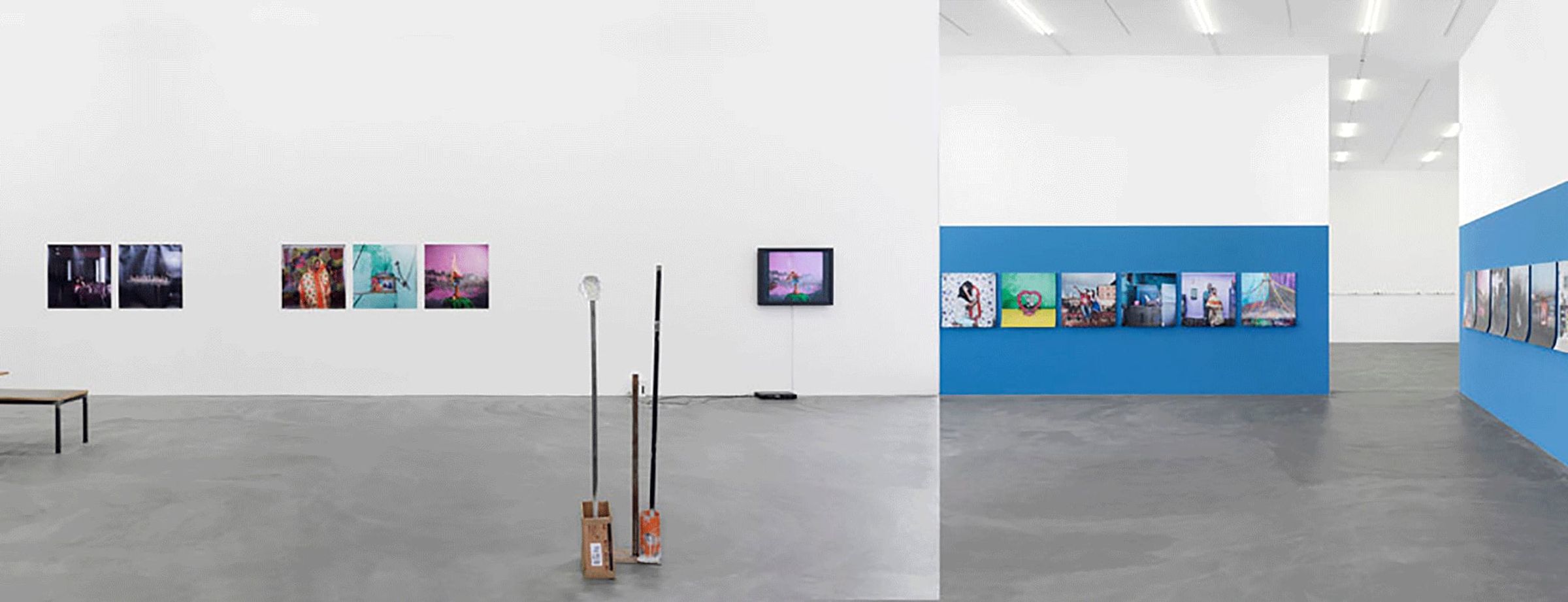 Wide gallery installation showing photographs, objects, and a blue wall of framed works.