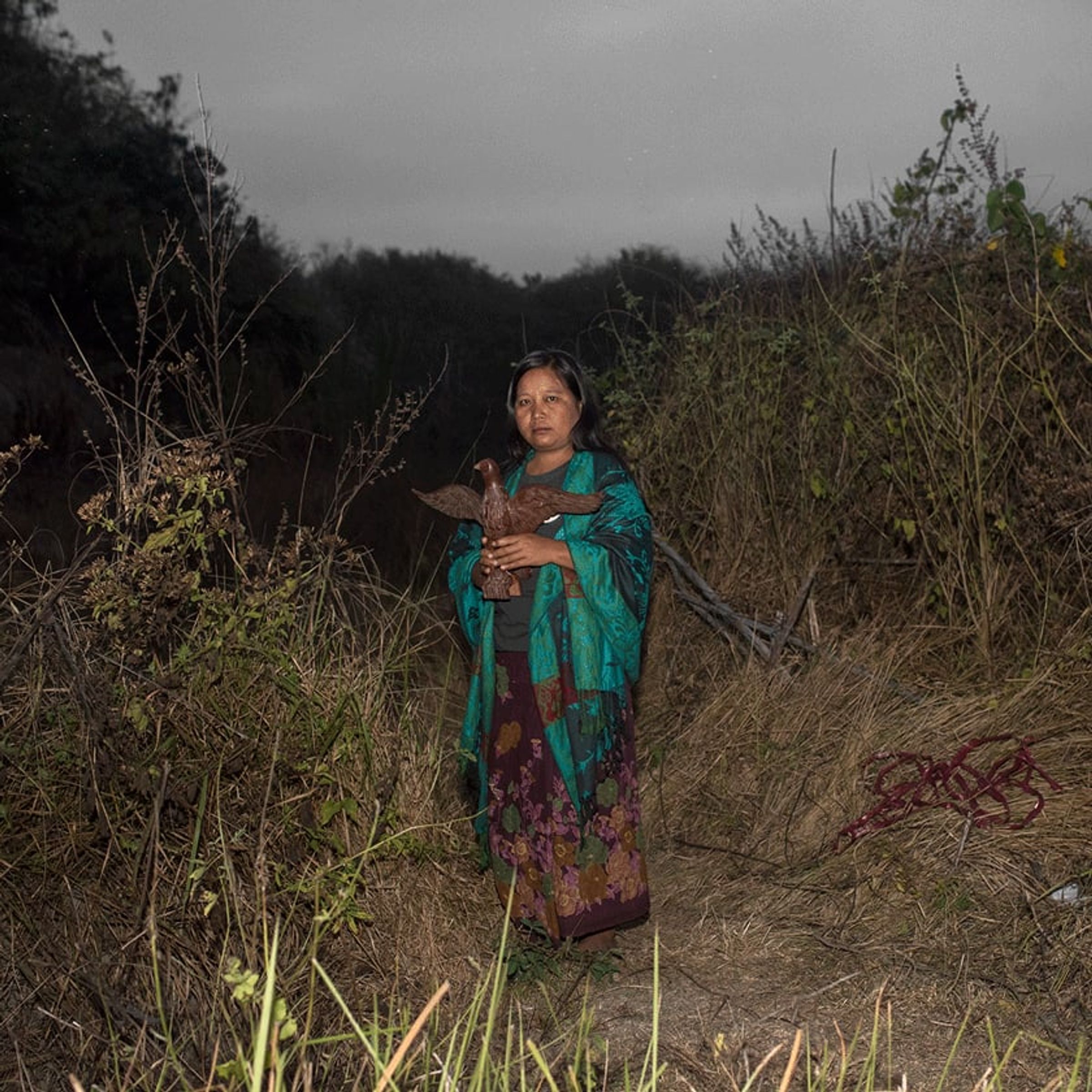 Person in green patterned clothing holds a coil of red cord among dry brush.