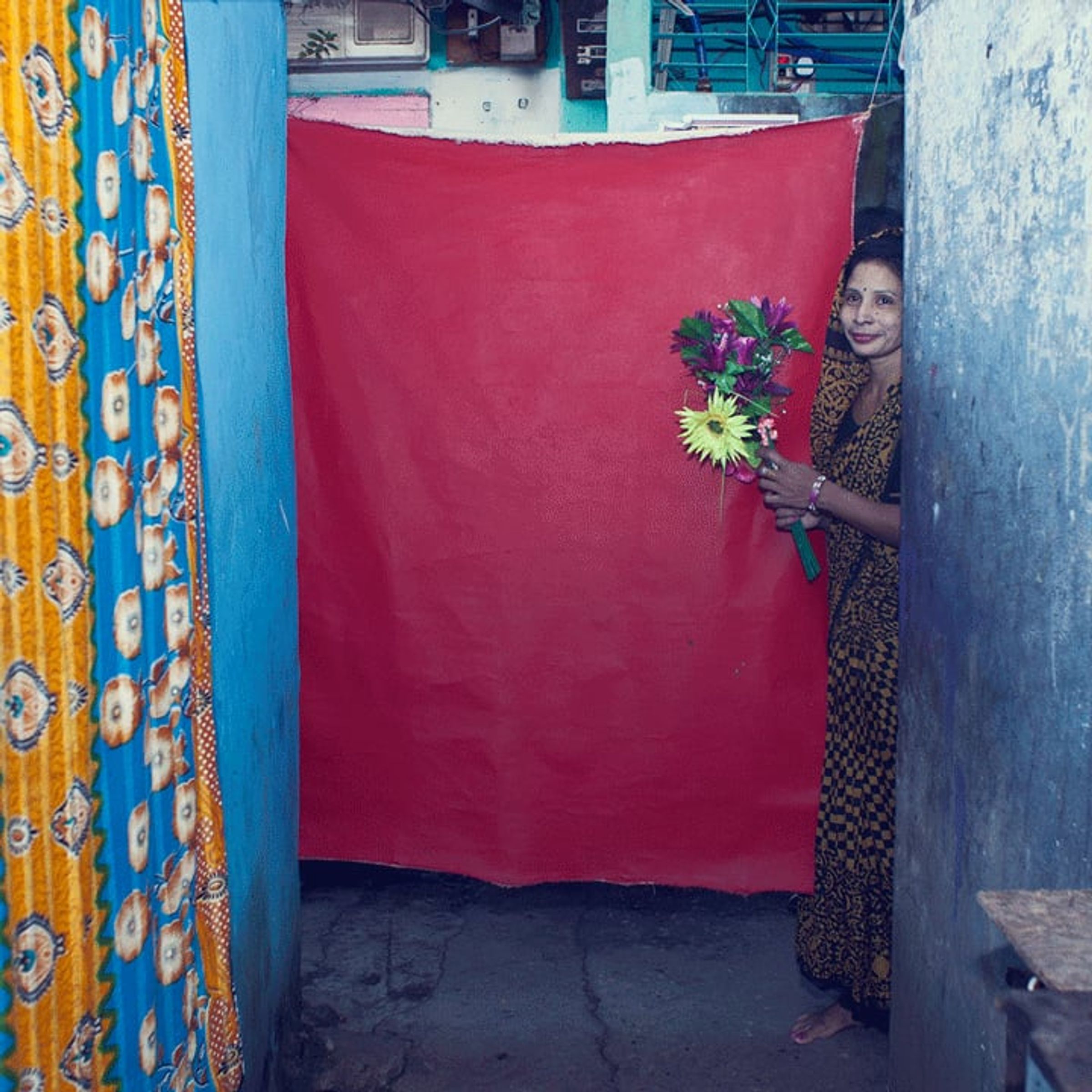 Older person holding a colorful bouquet leans into frame beside the red backdrop.