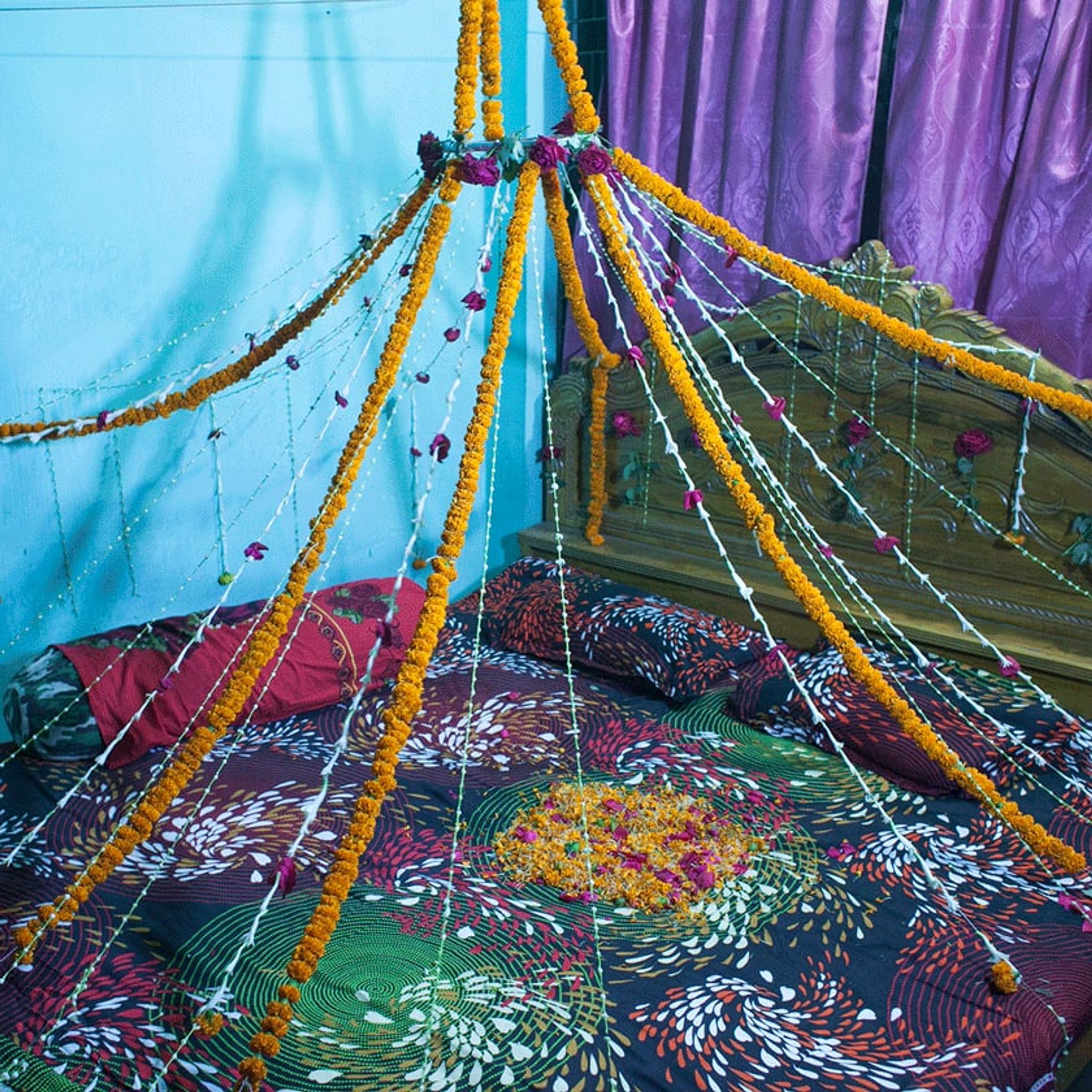 Flower garlands and strings form a canopy above a patterned bed.