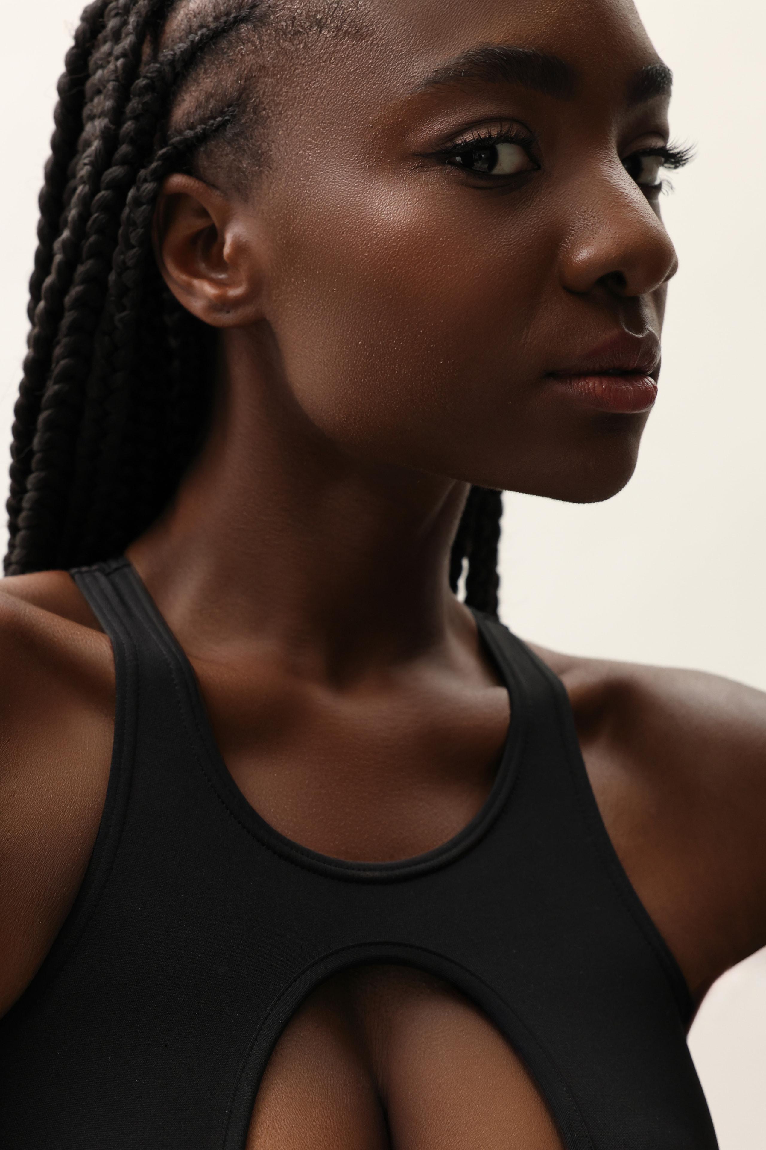 Close profile of woman with long braids in black racerback top against pale studio backdrop