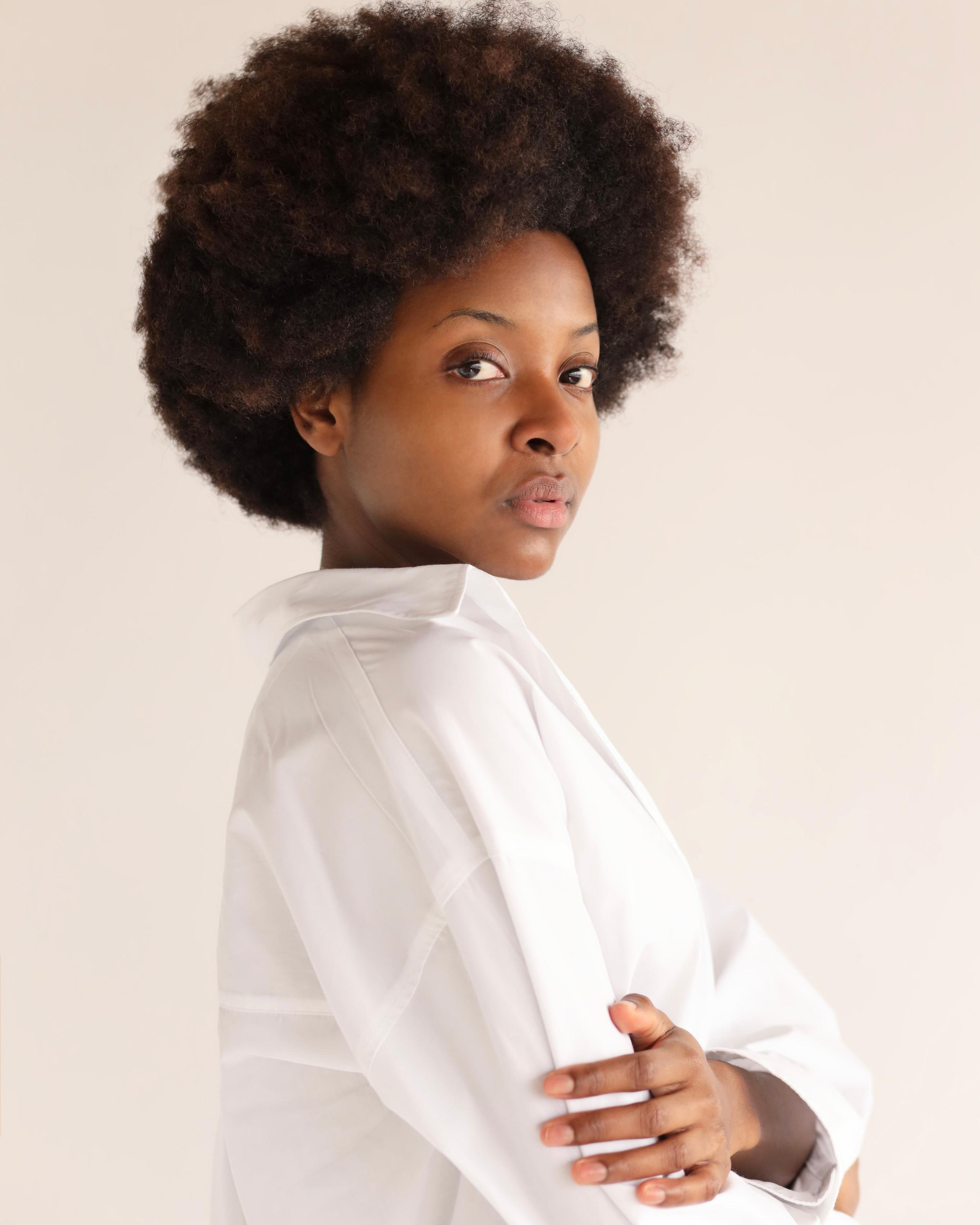 Black woman with voluminous afro in white shirt, glancing over shoulder against soft grey backdrop