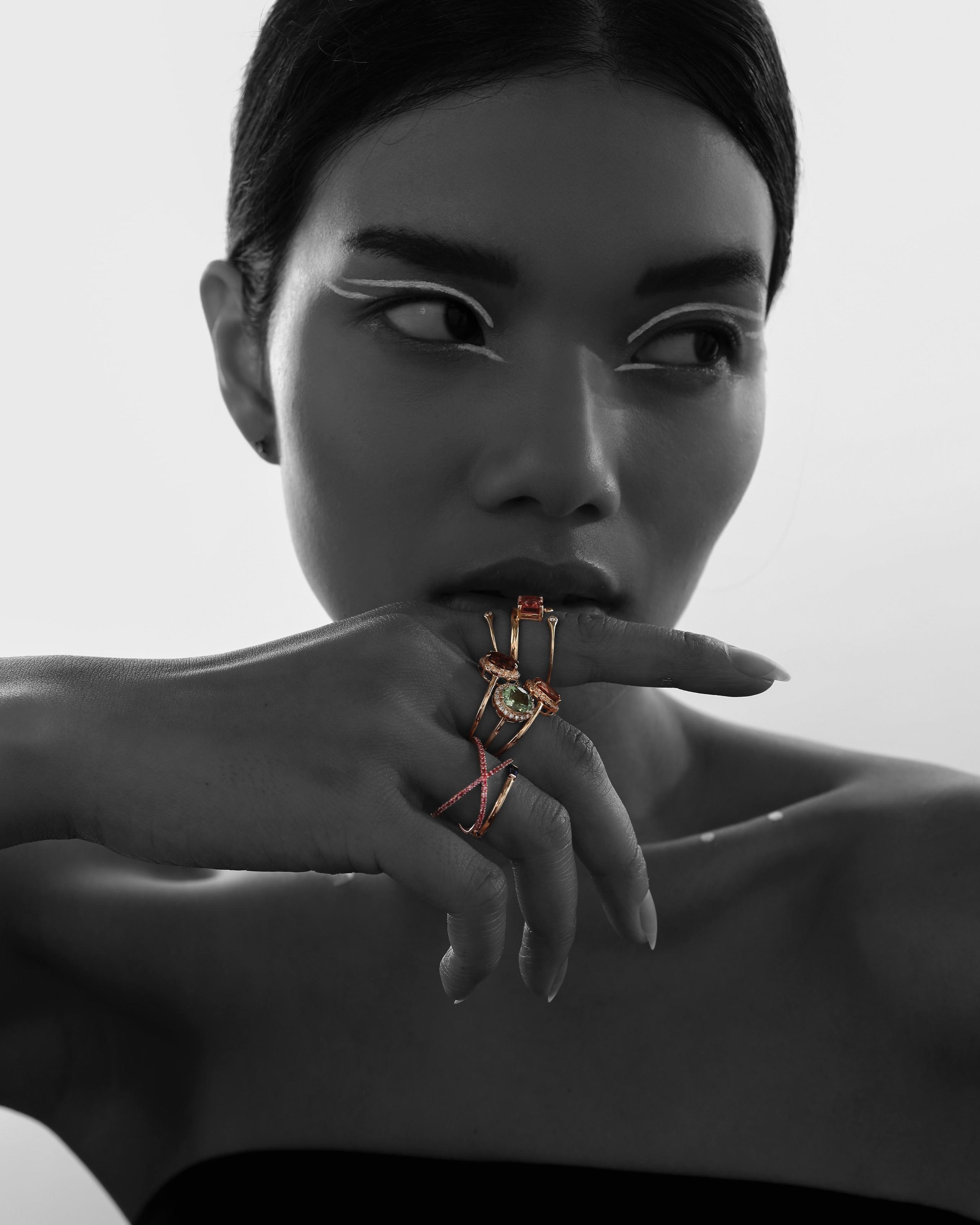 Black-and-white portrait with gemstone rings on the hand selectively colored gold and red.