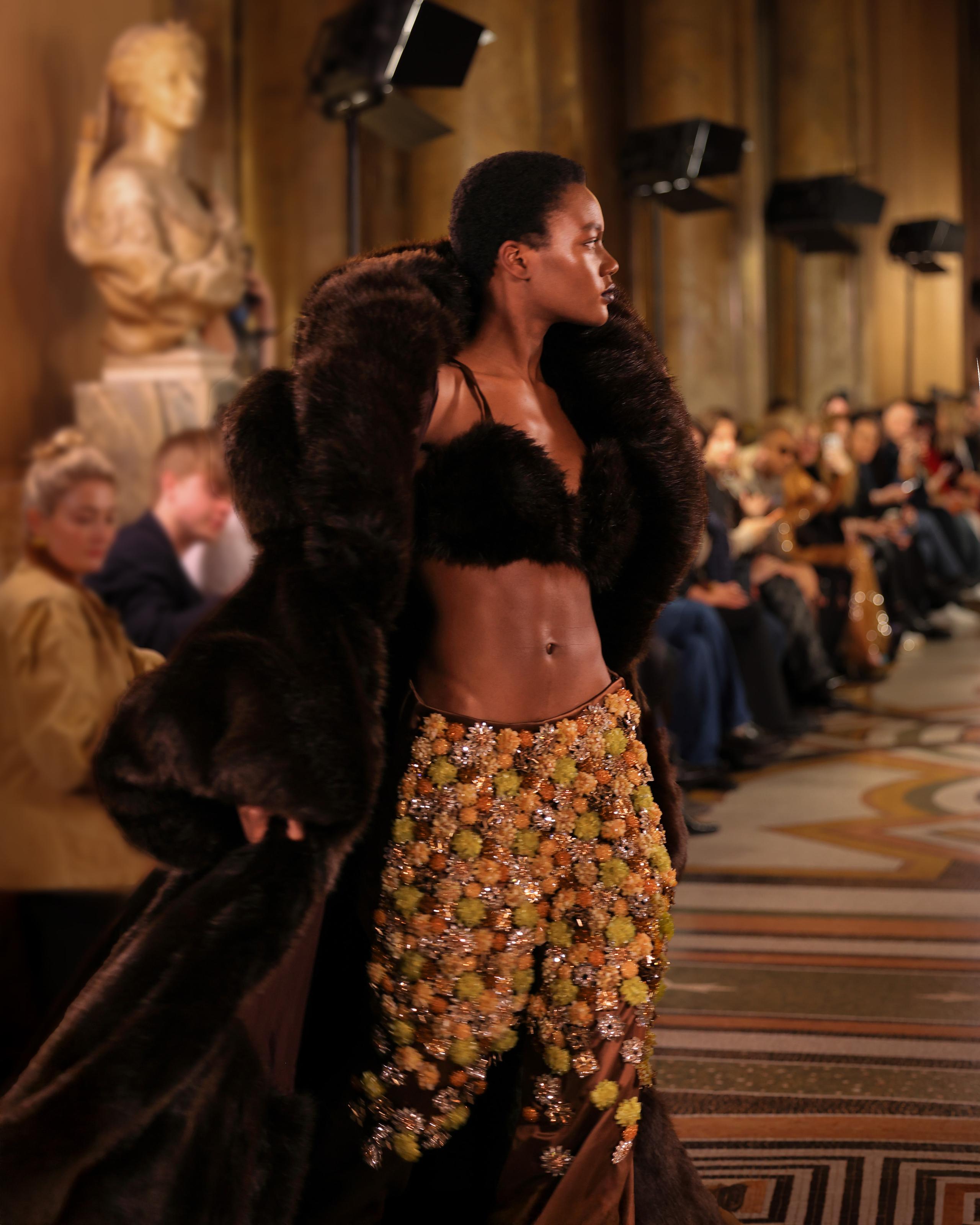 Profile of model in brown fur coat and shimmering beaded skirt on runway