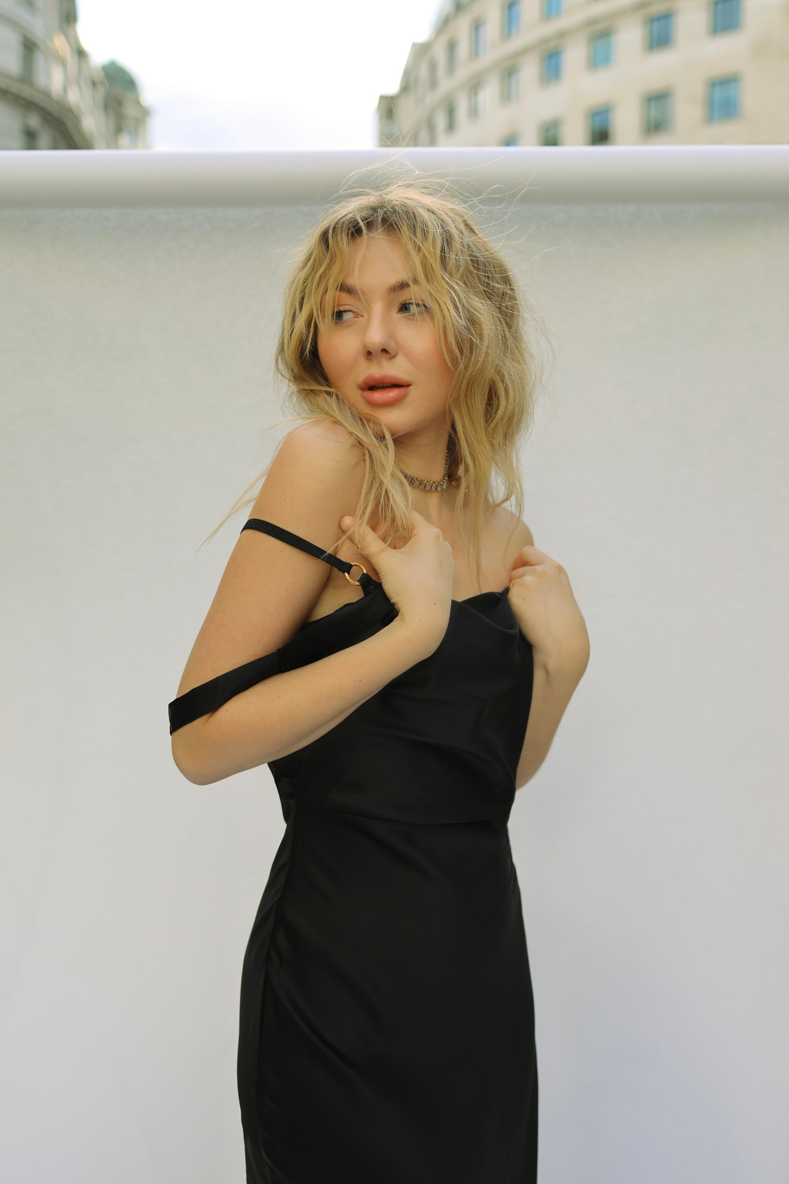 Blonde model in black silk slip dress glancing over shoulder against pale outdoor wall