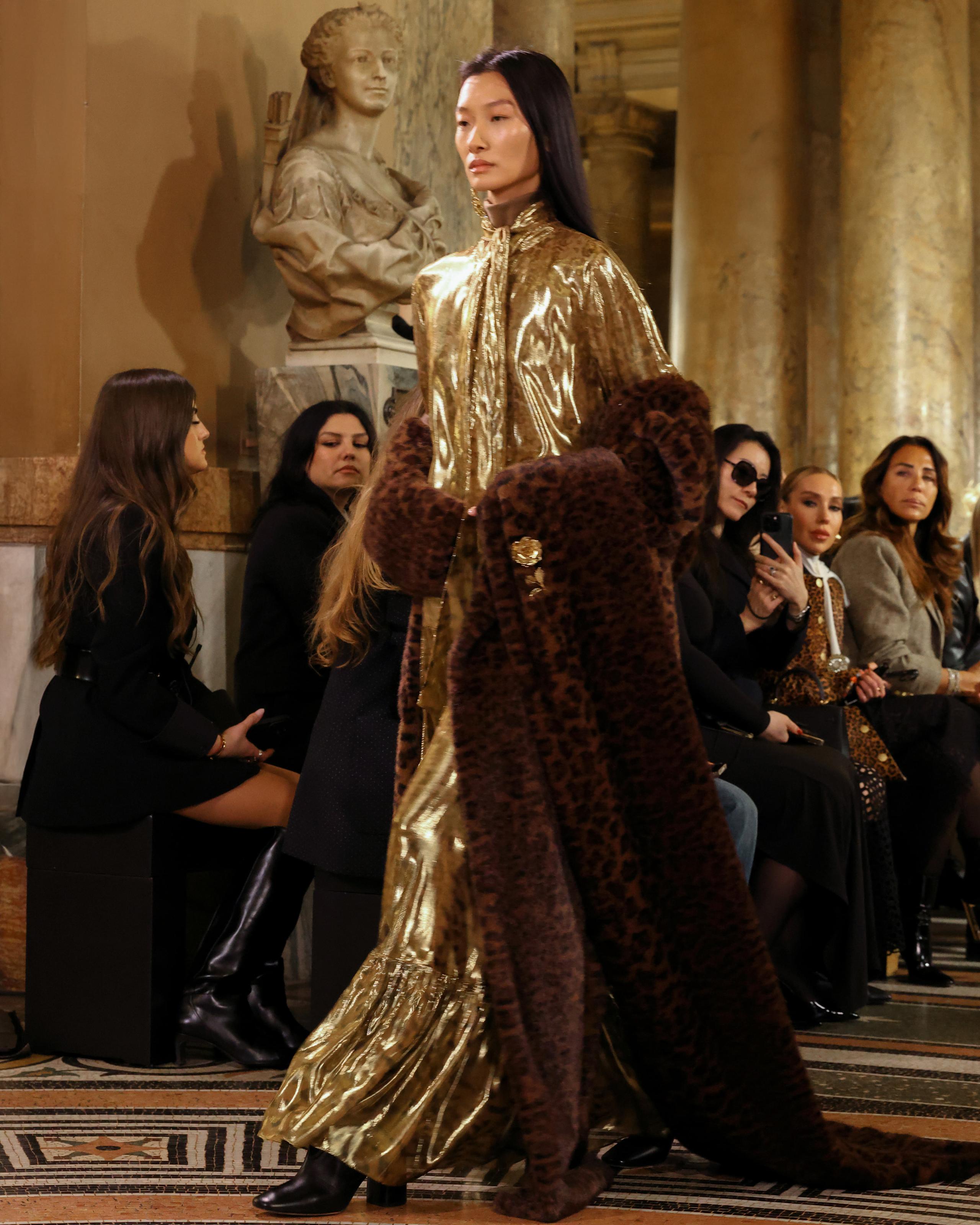 Model in shimmering gold gown and leopard fur stole on ornate marble runway