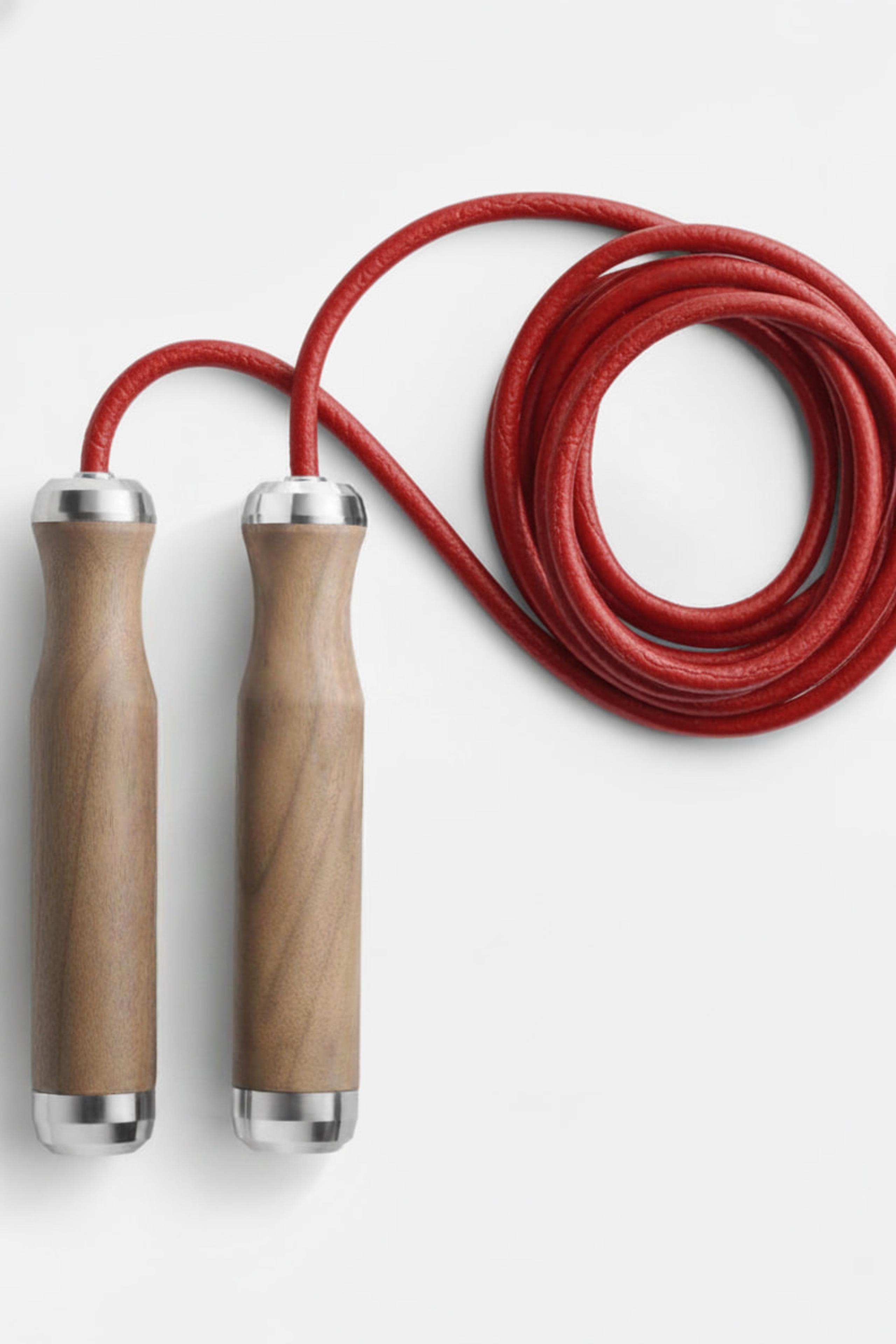 Coiled red leather skipping rope with wooden handles arranged on a pale grey surface, soft daylight.