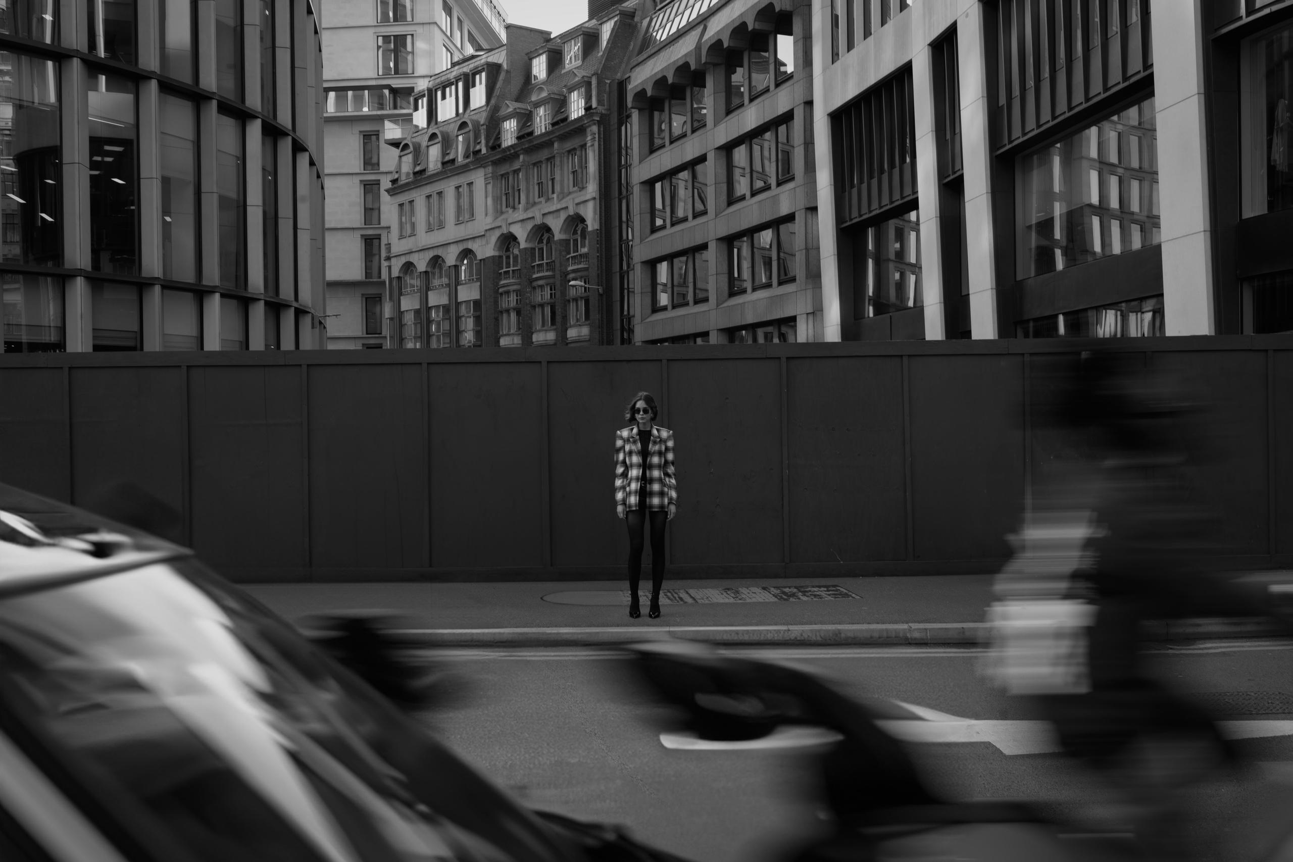 Monochrome wide shot of small figure in plaid blazer behind motion-blurred passing traffic in city