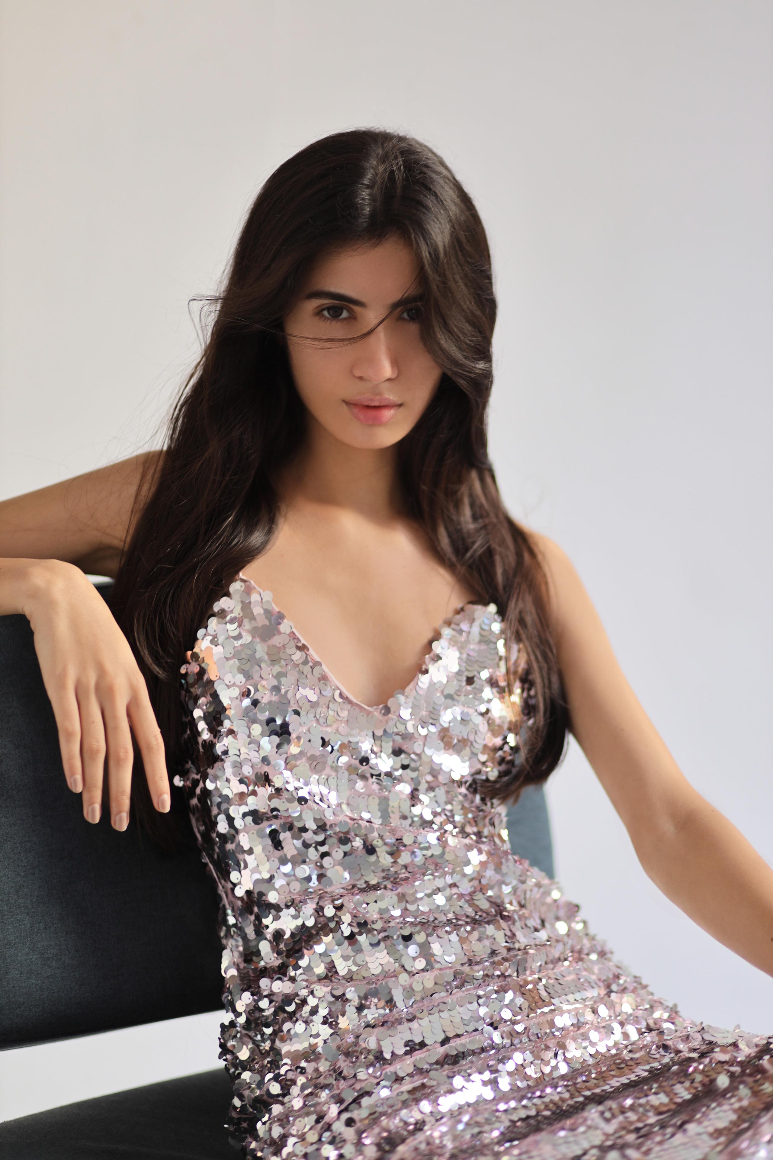 Seated woman in silver-pink sequin dress, long dark hair, soft daylight, calm direct gaze
