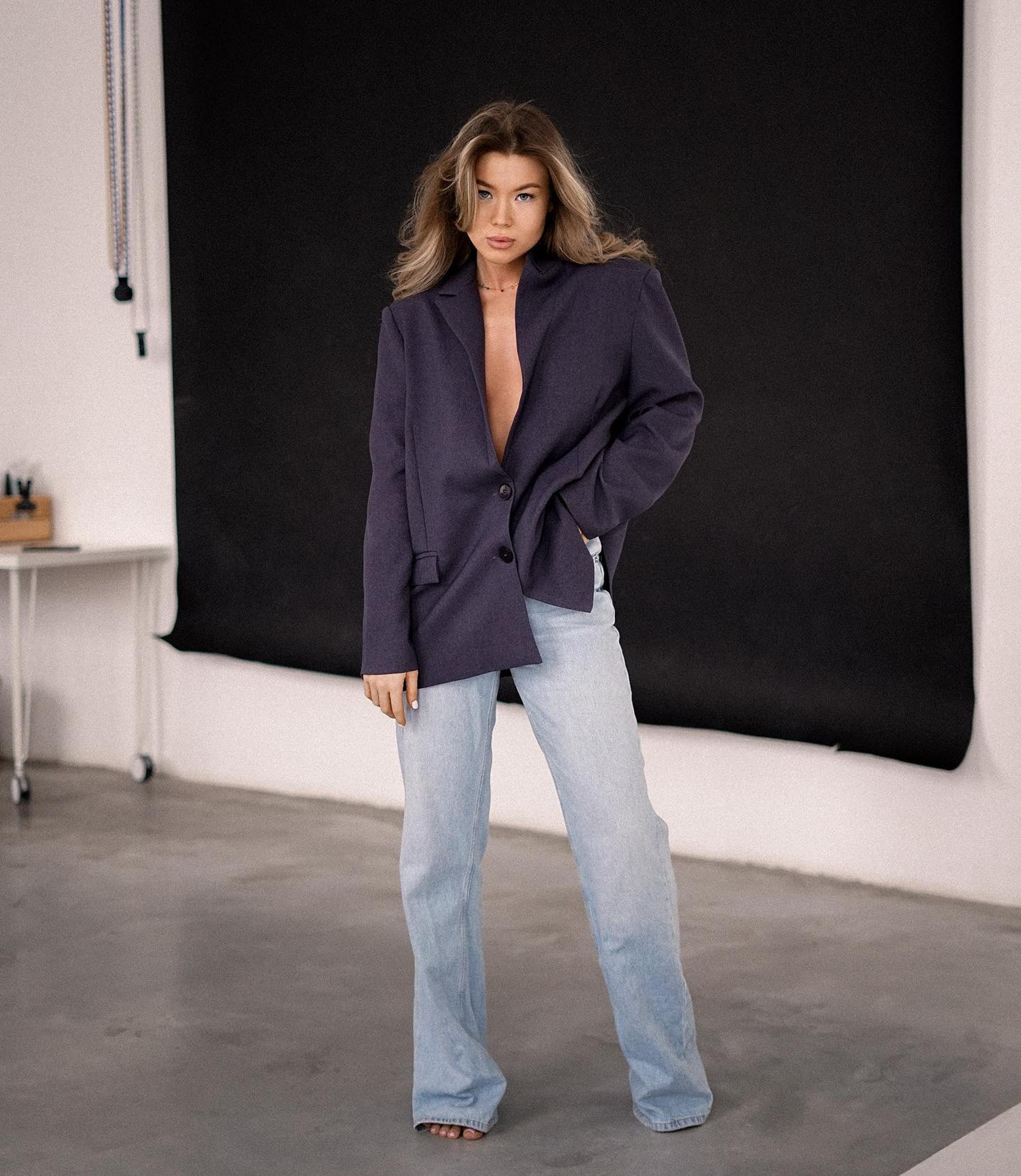 Blonde model in plunging navy blazer and faded jeans against black backdrop in studio