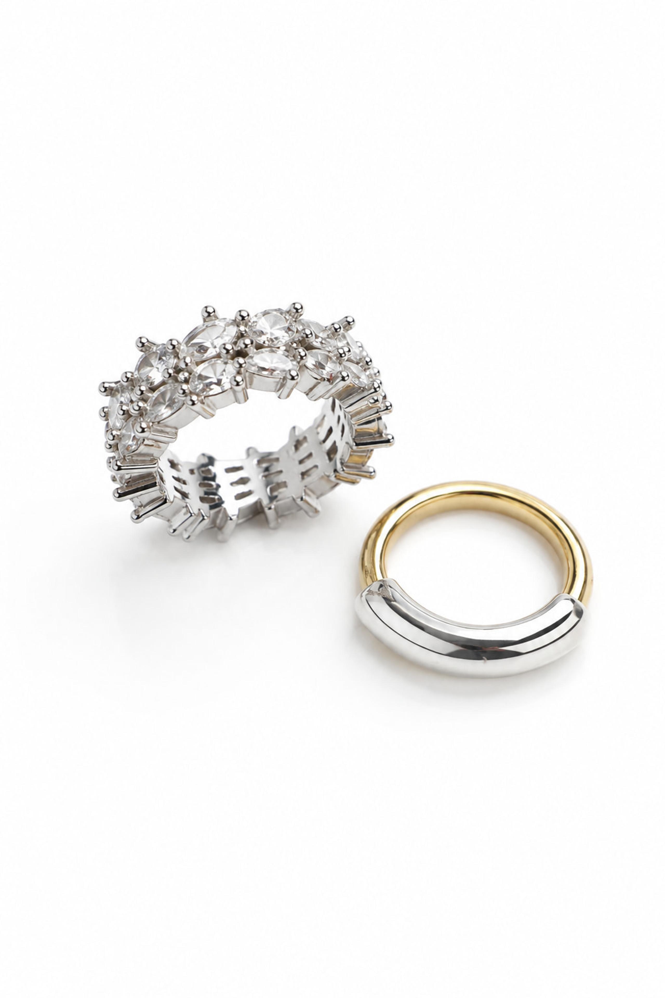 Crystal-encrusted silver ring beside a gold and silver two-tone band on white