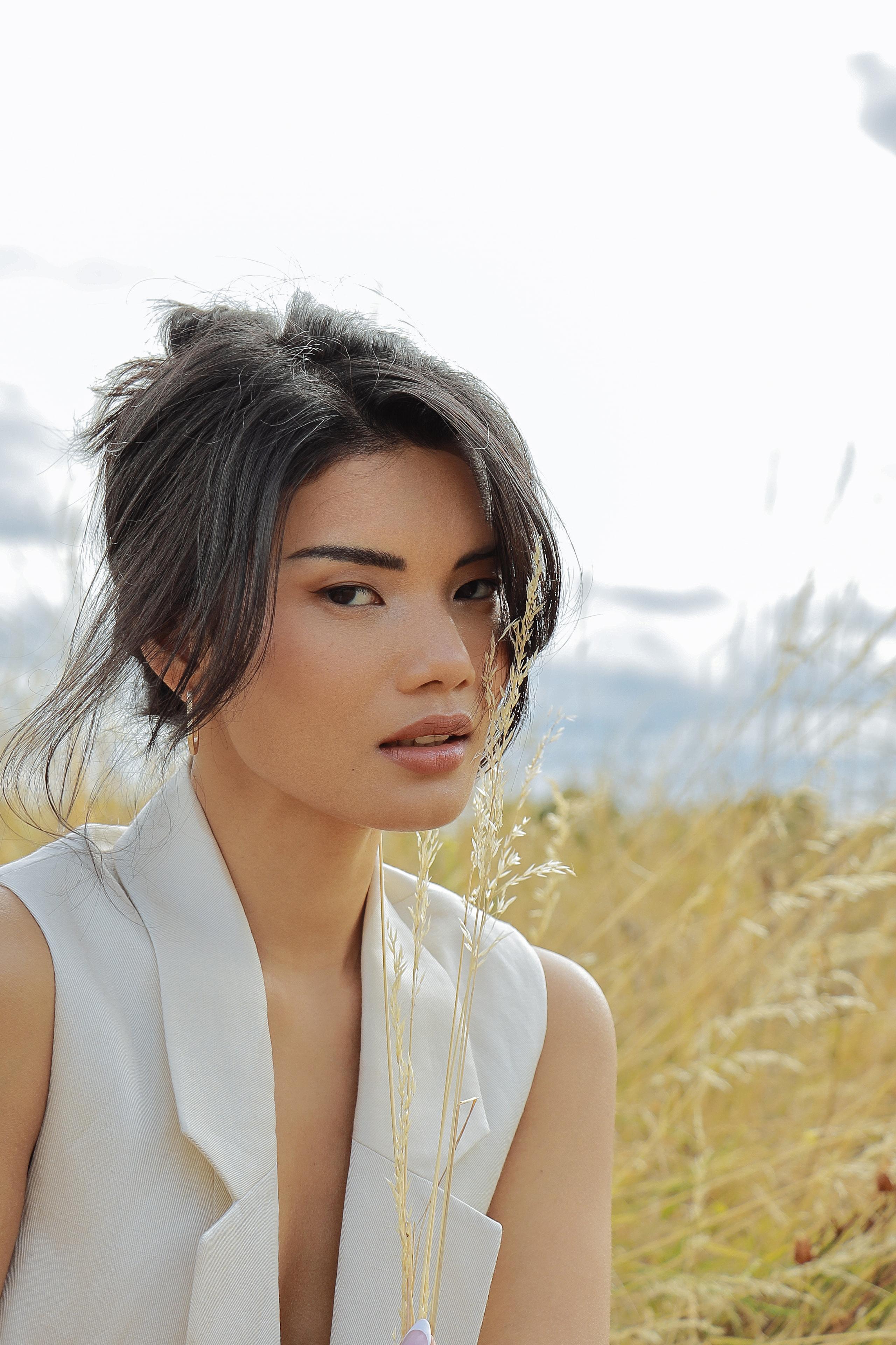 Woman in cream top in golden field, dried grass beside face, soft overcast daylight