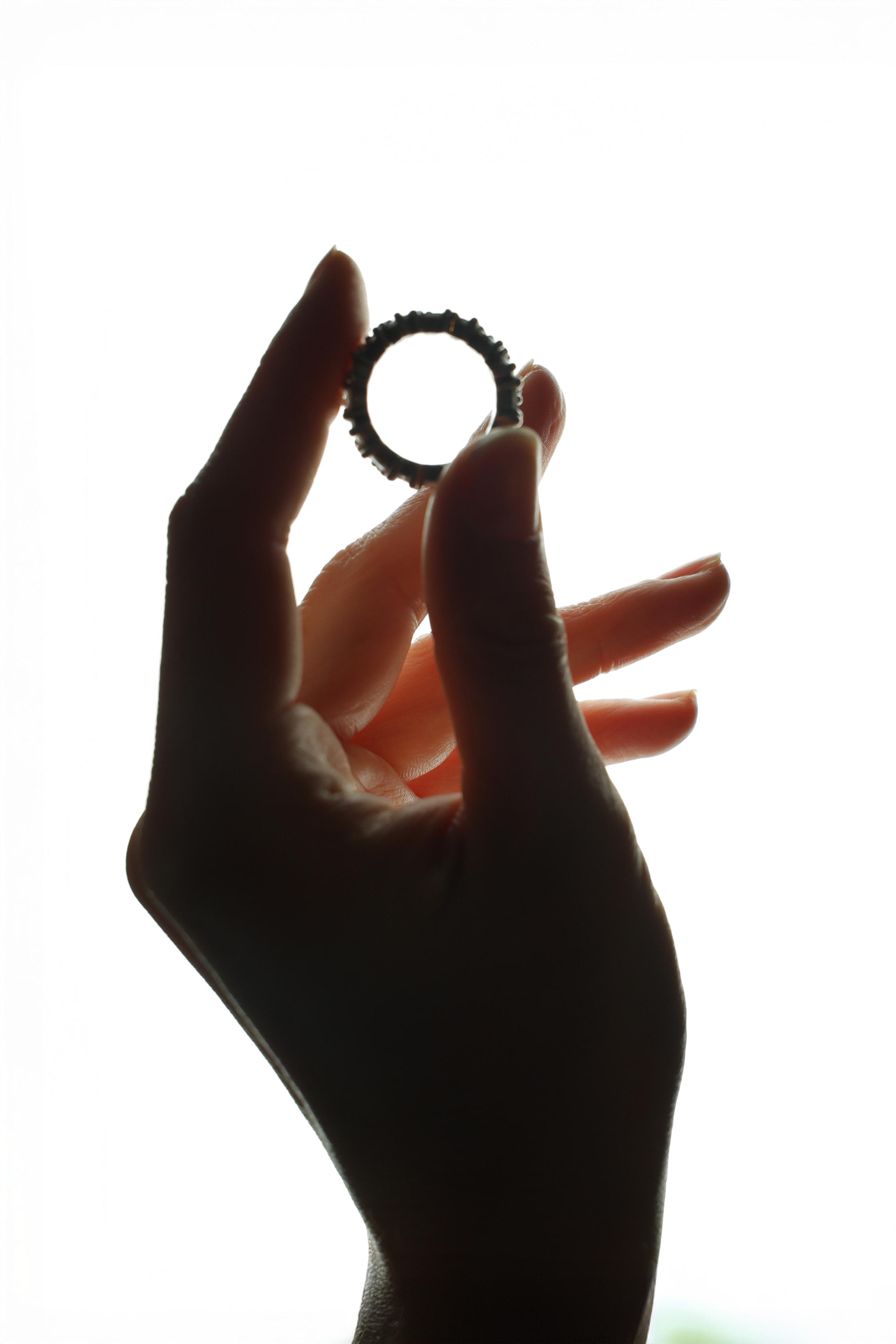 Hand silhouetted against bright sky holding a delicate eternity ring up to the light