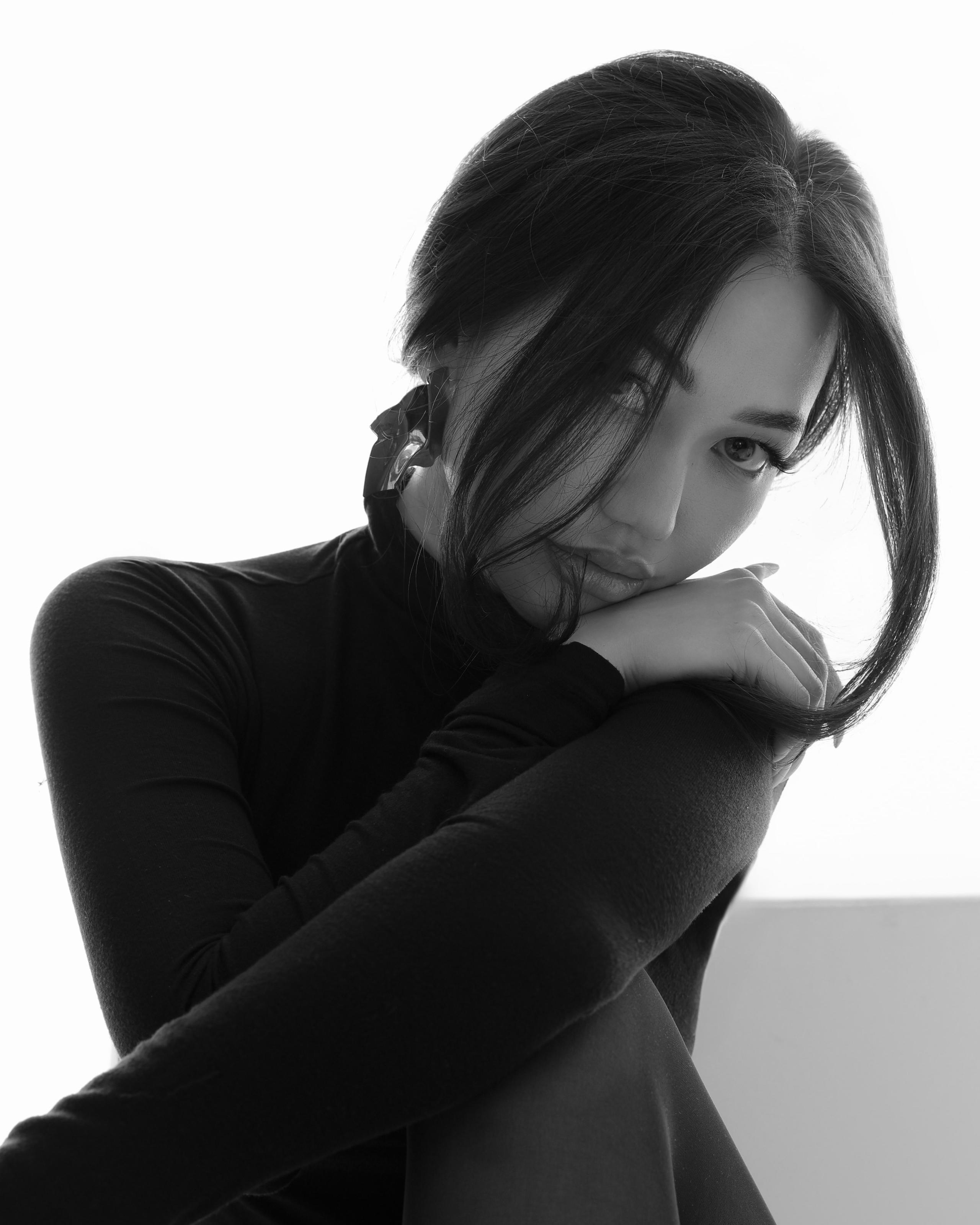 Black-and-white portrait of a woman in a turtleneck resting her chin on her arm, gazing softly aside