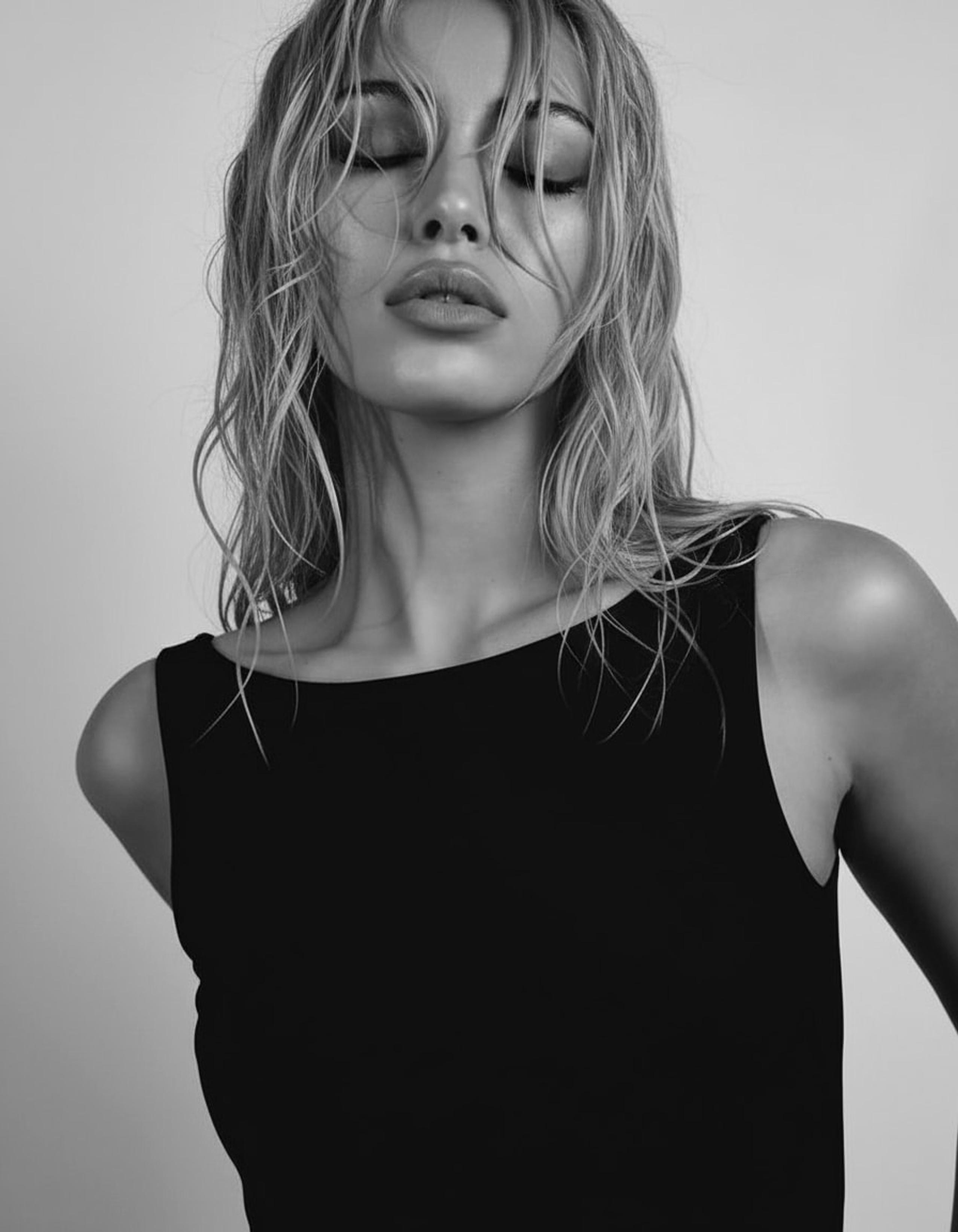 Close beauty portrait of blonde woman with wet-look hair, eyes closed, in black tank top