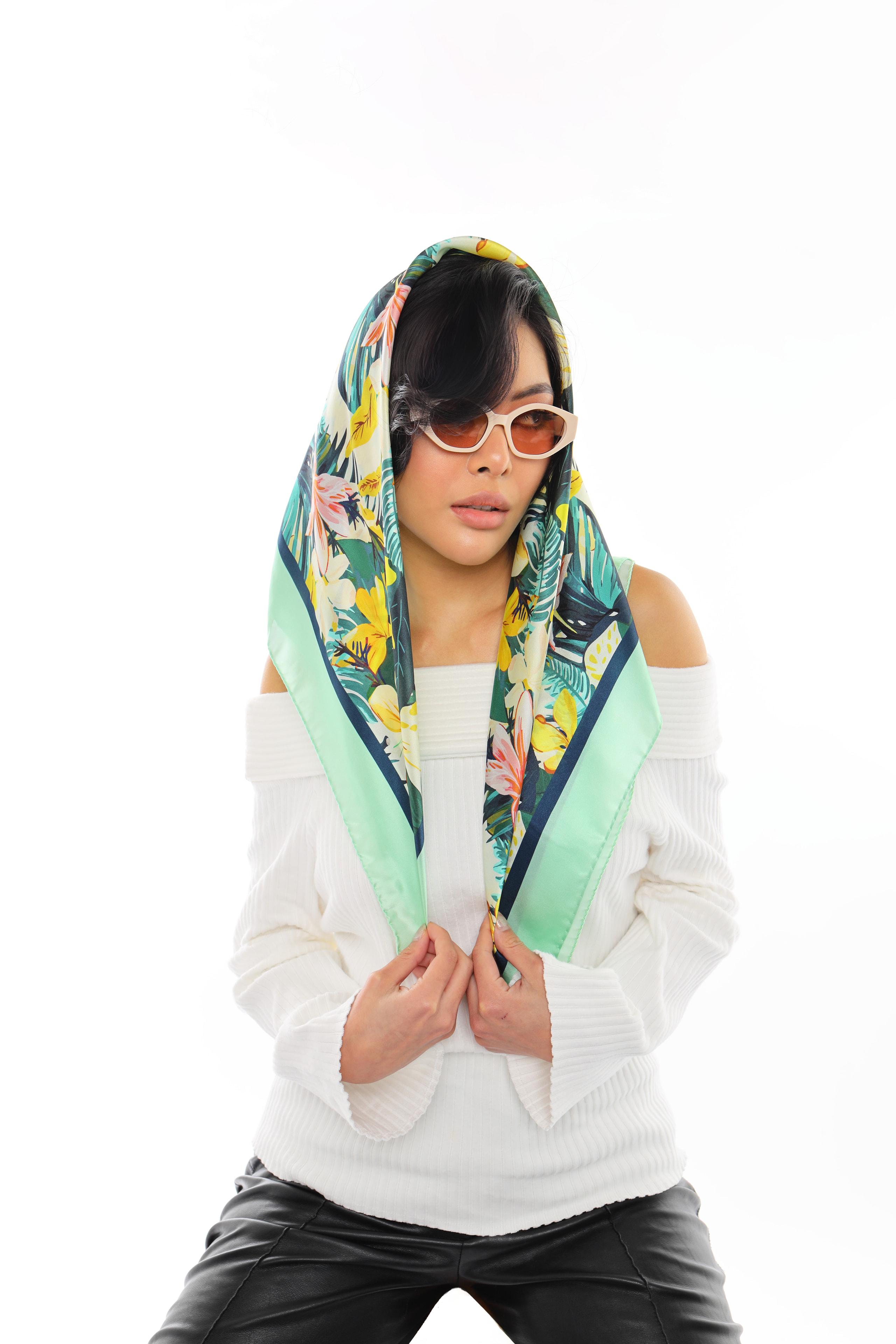 Woman draping a tropical floral silk scarf over her head like a hood with sunglasses and white top.