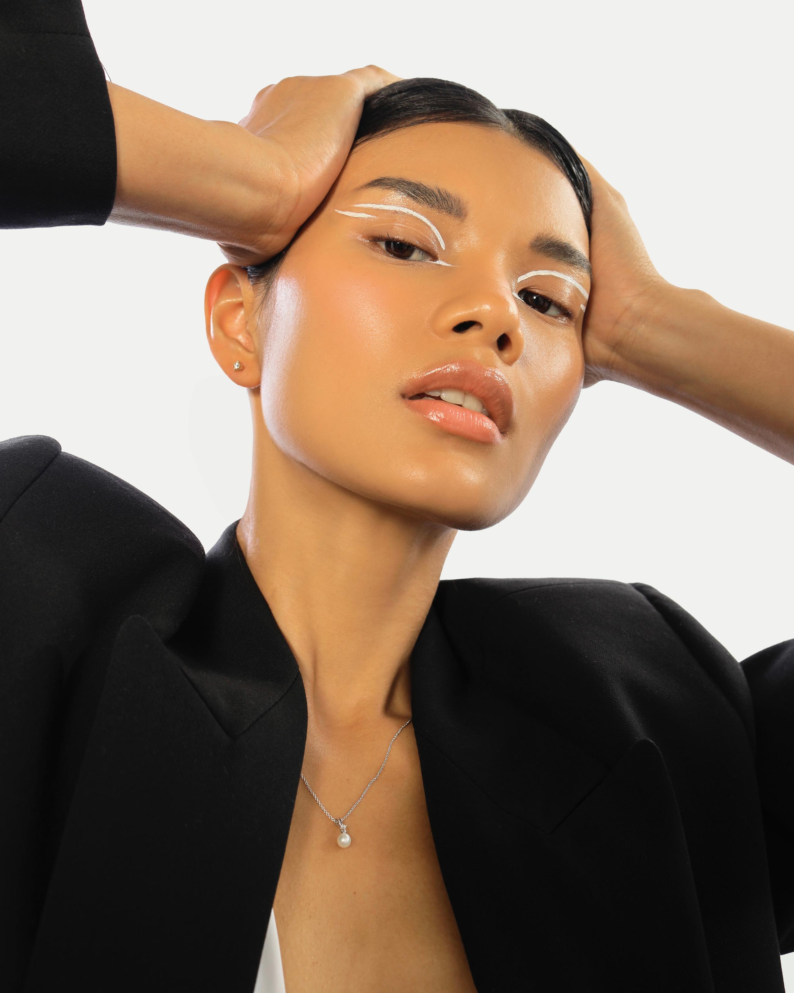 Beauty portrait of a woman in a black blazer with graphic white eyeliner and a pearl pendant necklace.