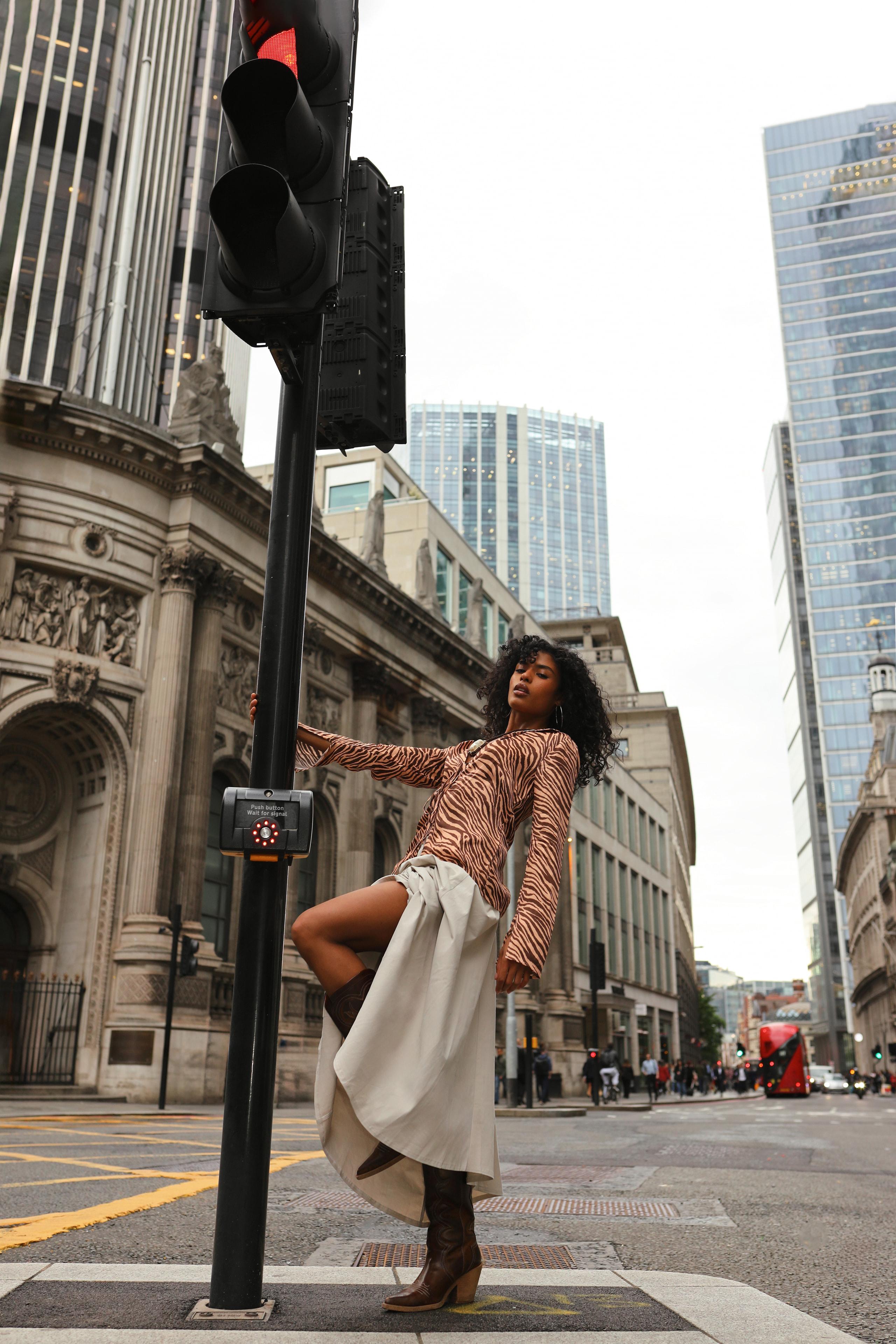 Model in tiger-print top leans from a traffic pole on a London City street at dusk