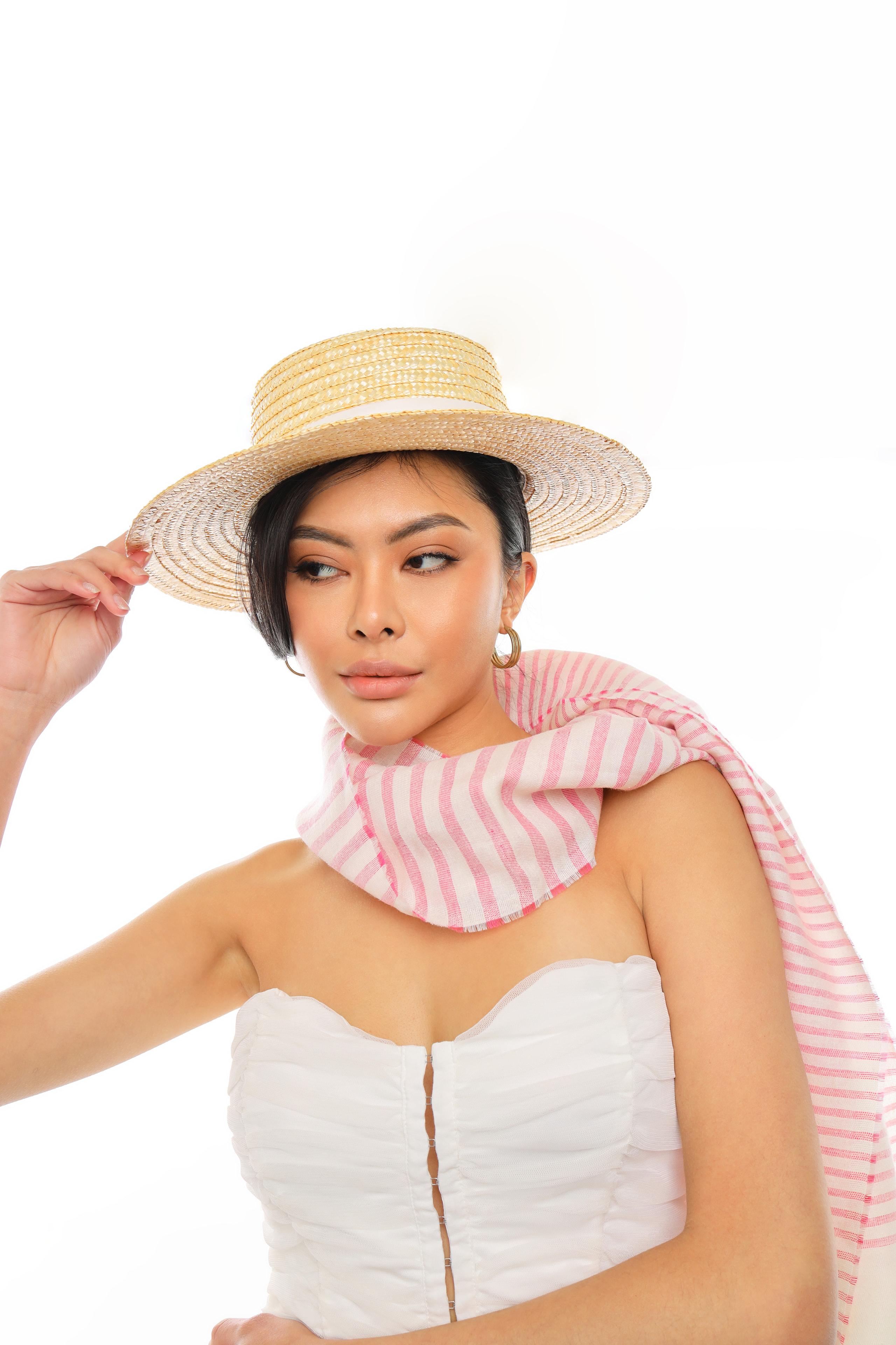 Woman in a straw boater hat and pink striped scarf with a white strapless ruched top.