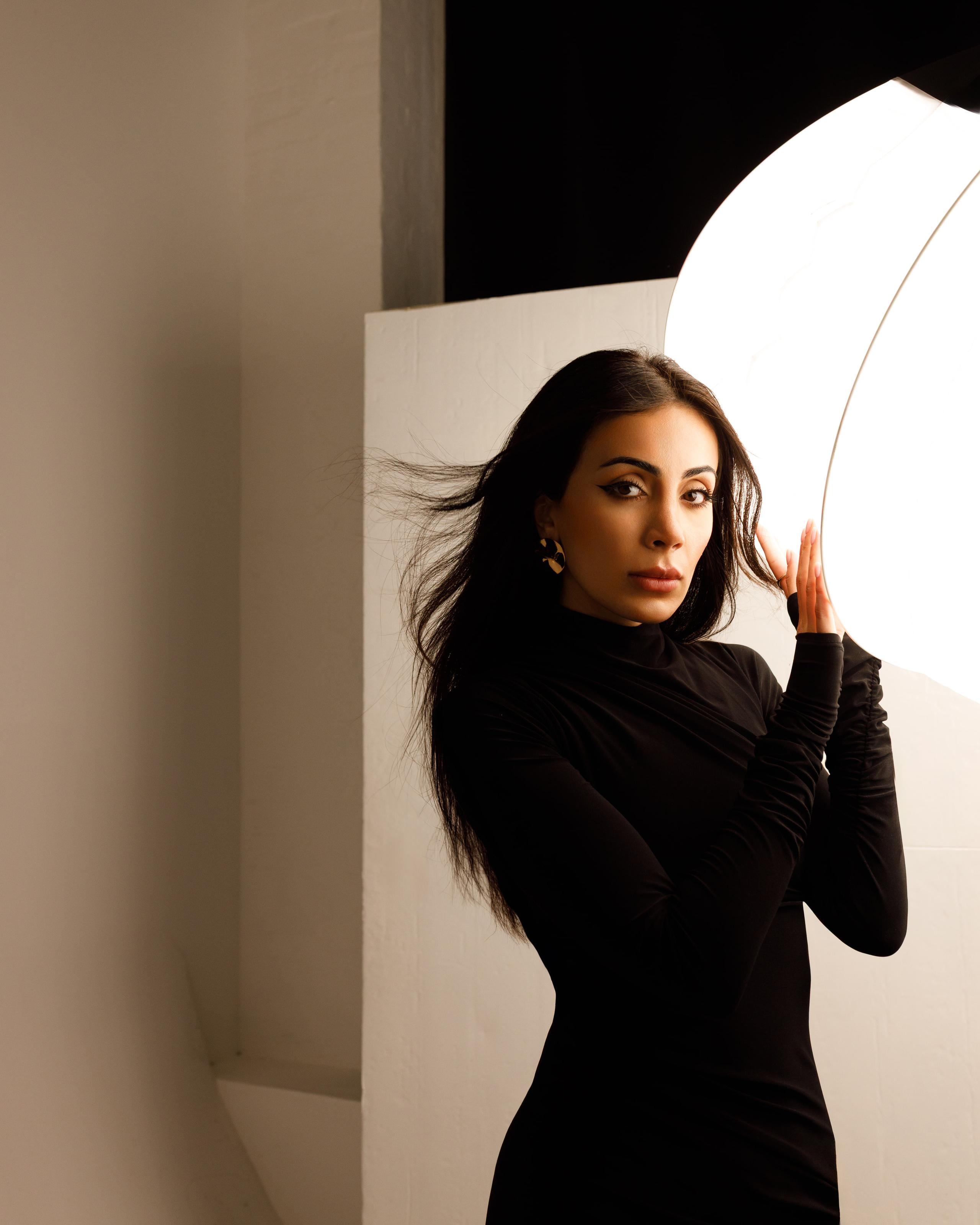 Brunette model in black turtleneck dress reaching toward a glowing round studio light