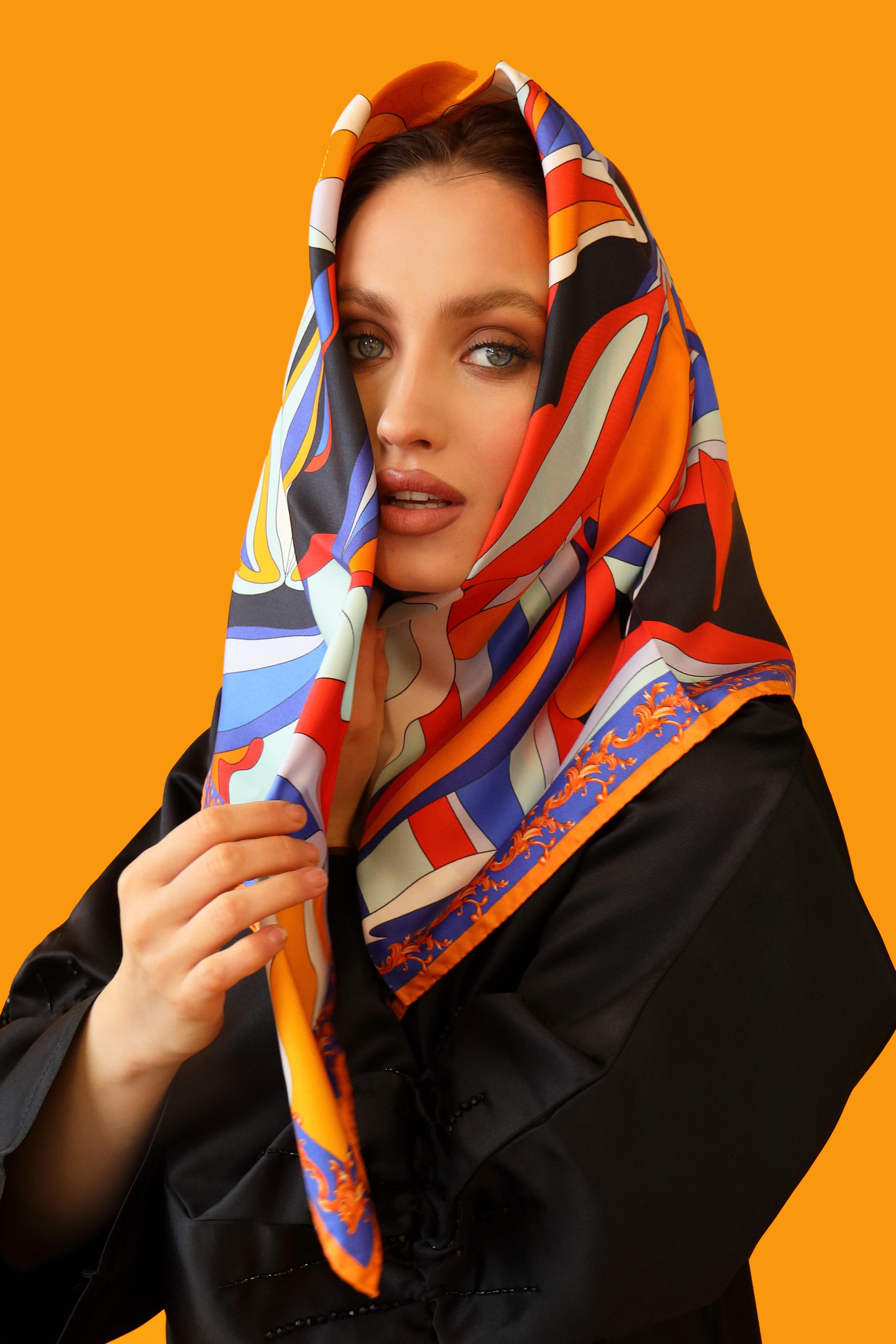 Model framing her face with a vivid orange and blue printed silk scarf headwrap