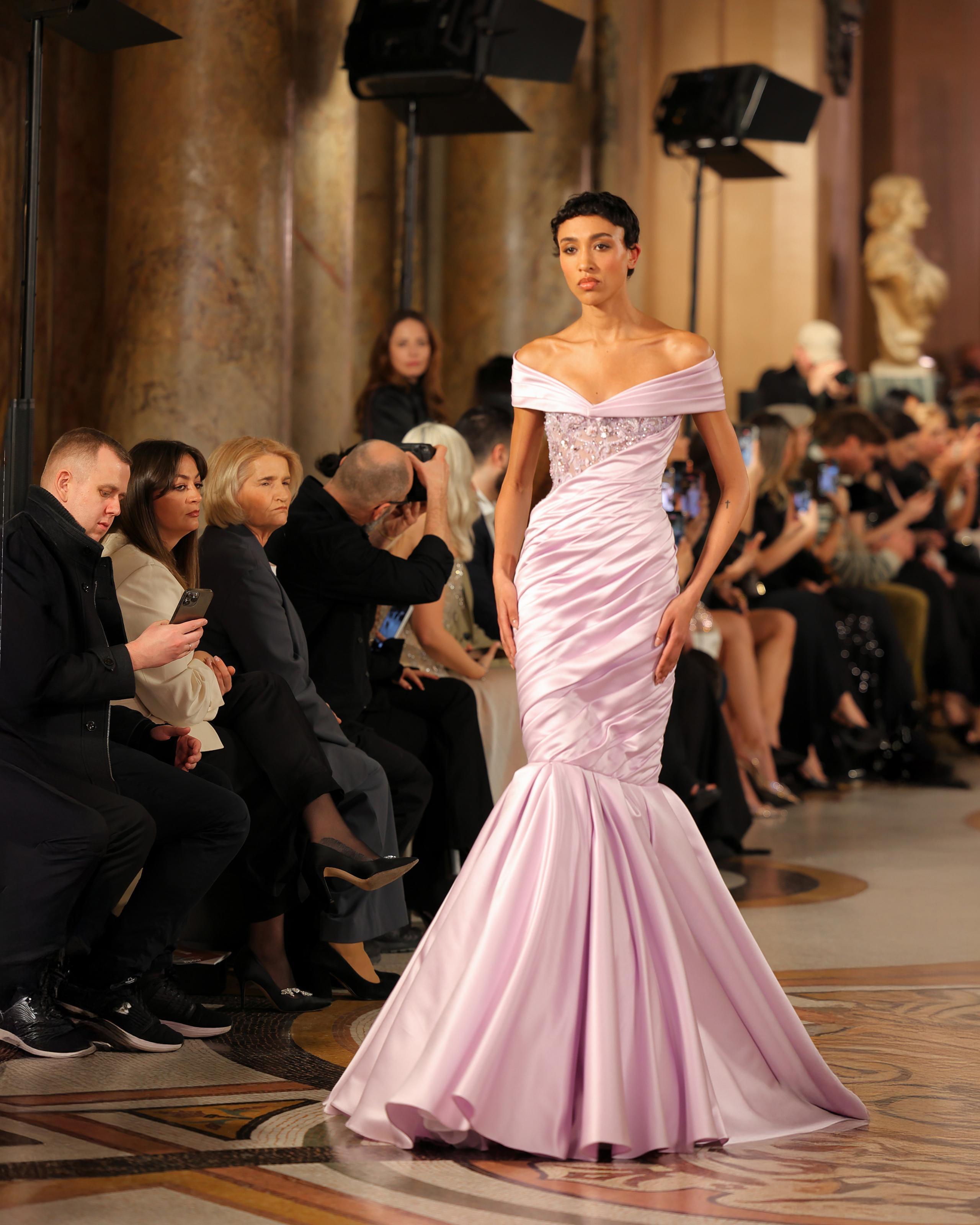 Model in off-shoulder lilac satin mermaid gown on patterned marble runway