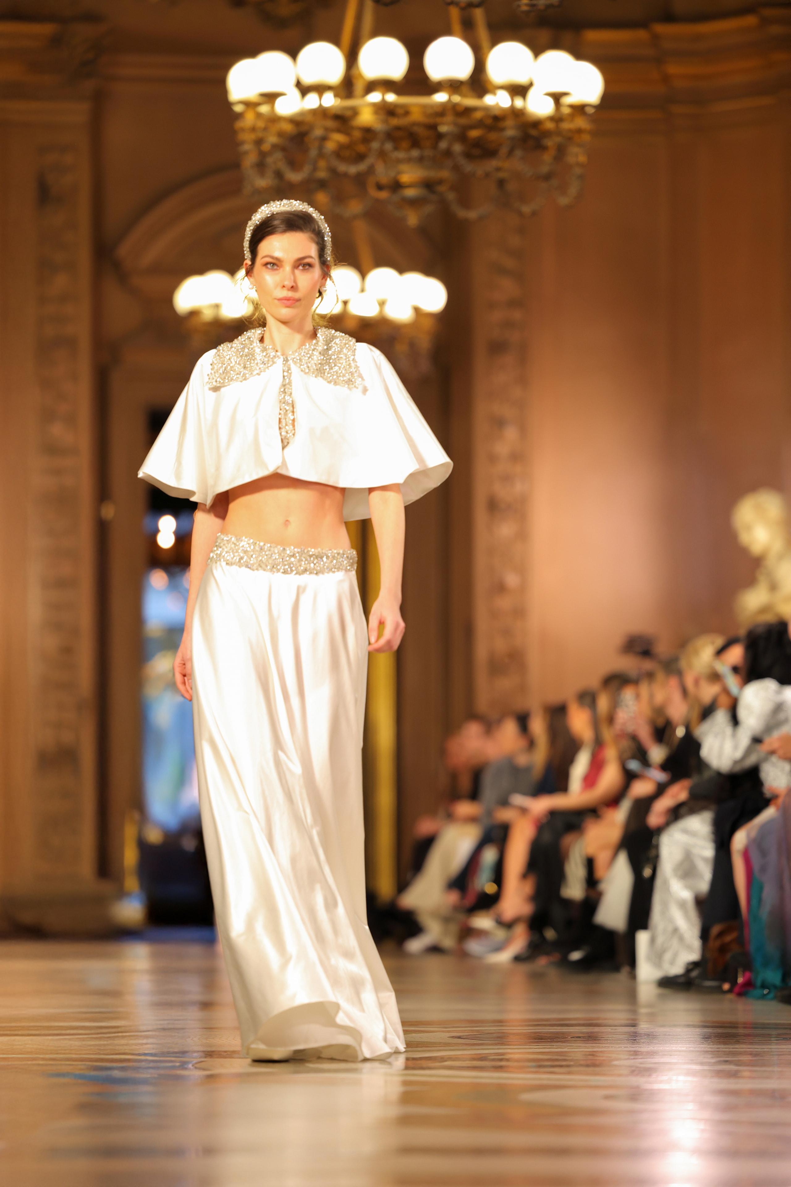 Model in ivory beaded crop cape and satin skirt walking grand chandelier runway