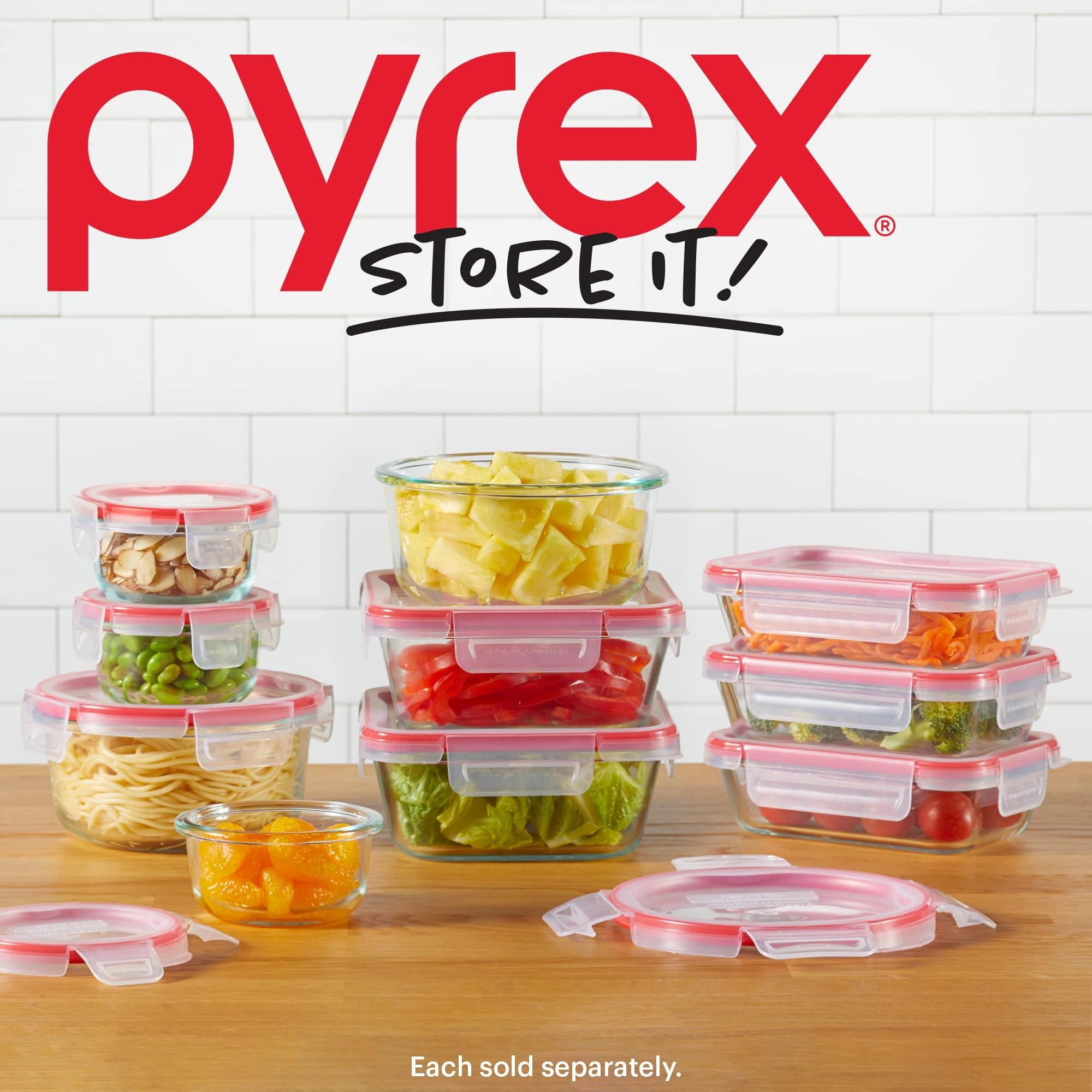 Alt text: Promotional image for Pyrex “Store It!” glass food storage containers arranged on a wooden countertop against a white tile background. Multiple clear containers with red lids are filled with foods like pineapple chunks, sliced red peppers, lettuce, noodles, peas, almonds, broccoli, cherry tomatoes, shredded carrots, and orange segments. The large red “pyrex” logo and black “STORE IT!” text appear at the top.