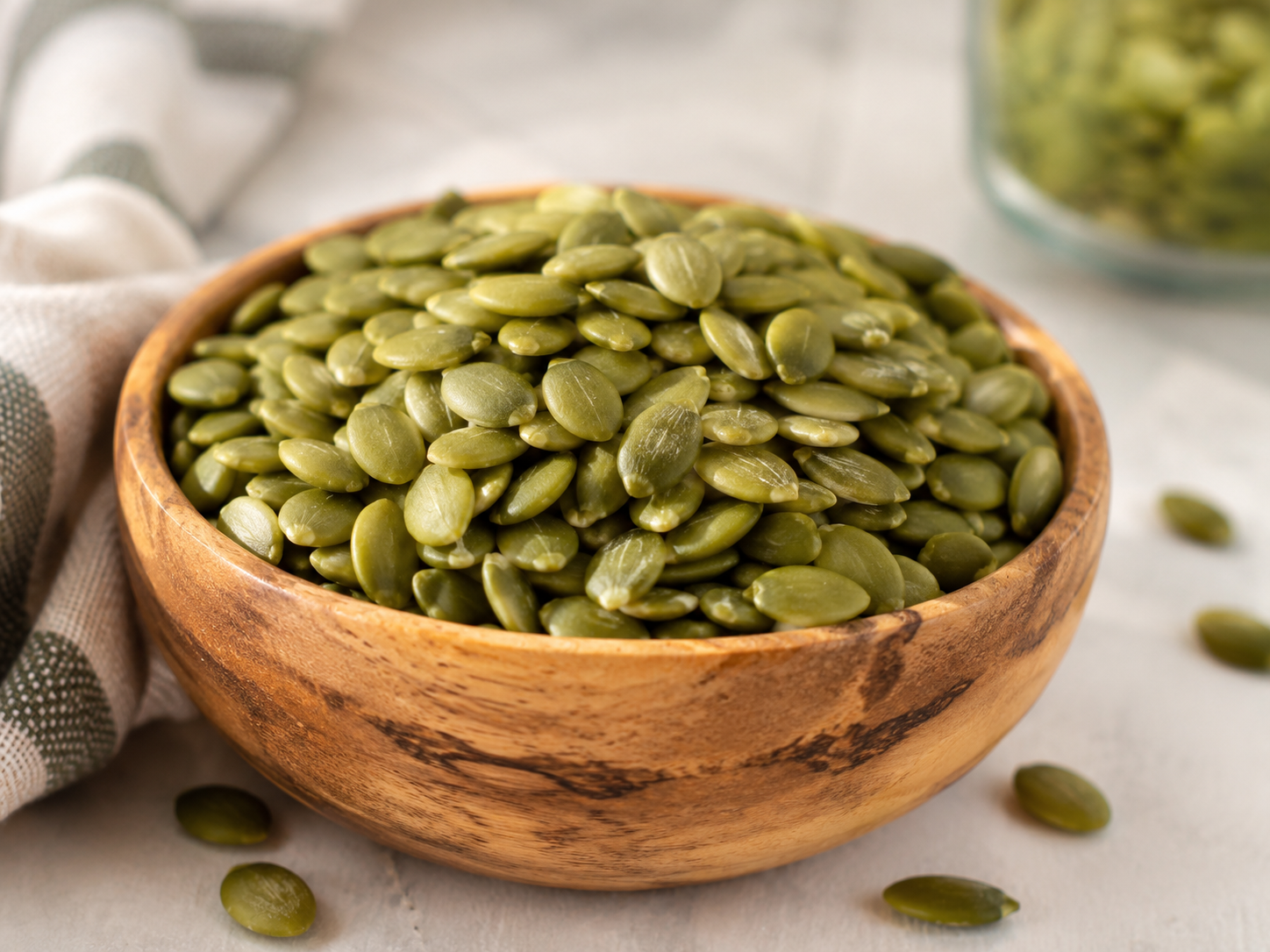 Raw unsalted green pumpkin seeds (pepitas) piled in a rustic wooden bowl on a light kitchen countertop before soaking.