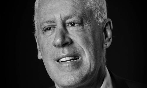 A black and white headshot of a man with white hair and wearing a suit