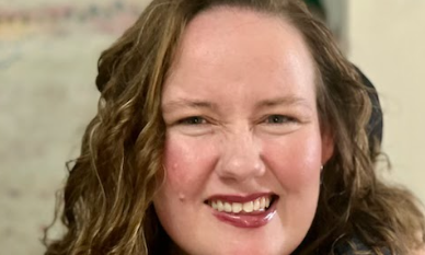 A headshot of C31 Chair Emily Dash - Emily a woman with long brown hair smiles at the camera.