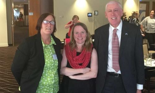 Three people at a conference are smiling at the camera
