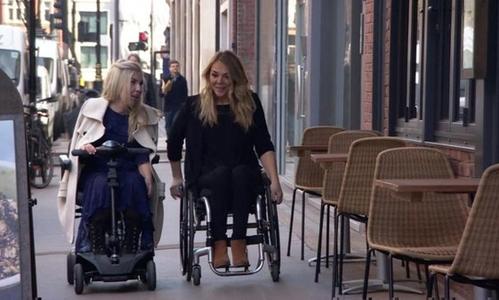 Two wheelchair users on the sidewalk talking