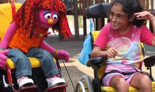 A life sized puppet and a child use wheelchairs side by side