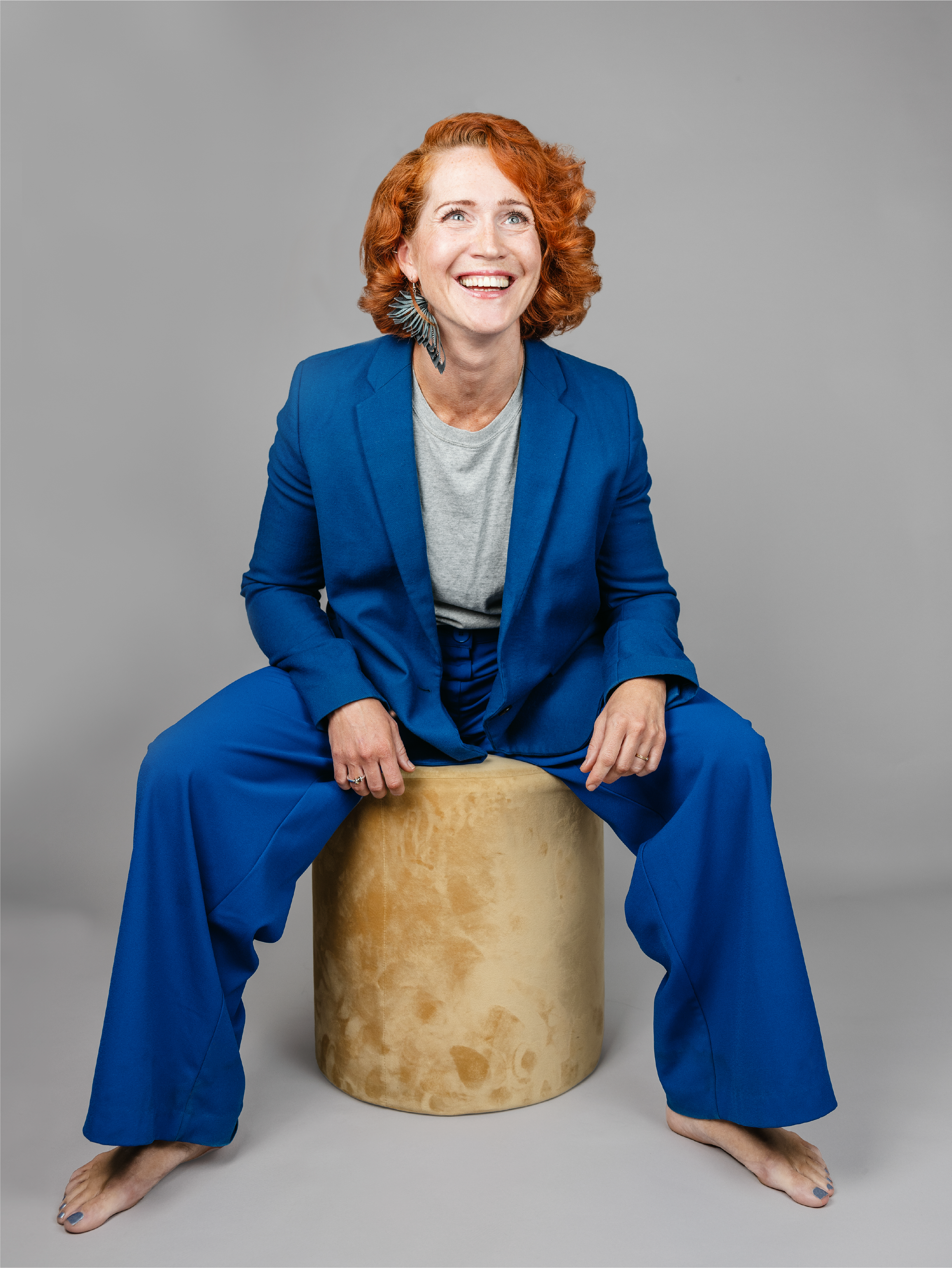 Woman with red hair in a blue suit sitting on a stool