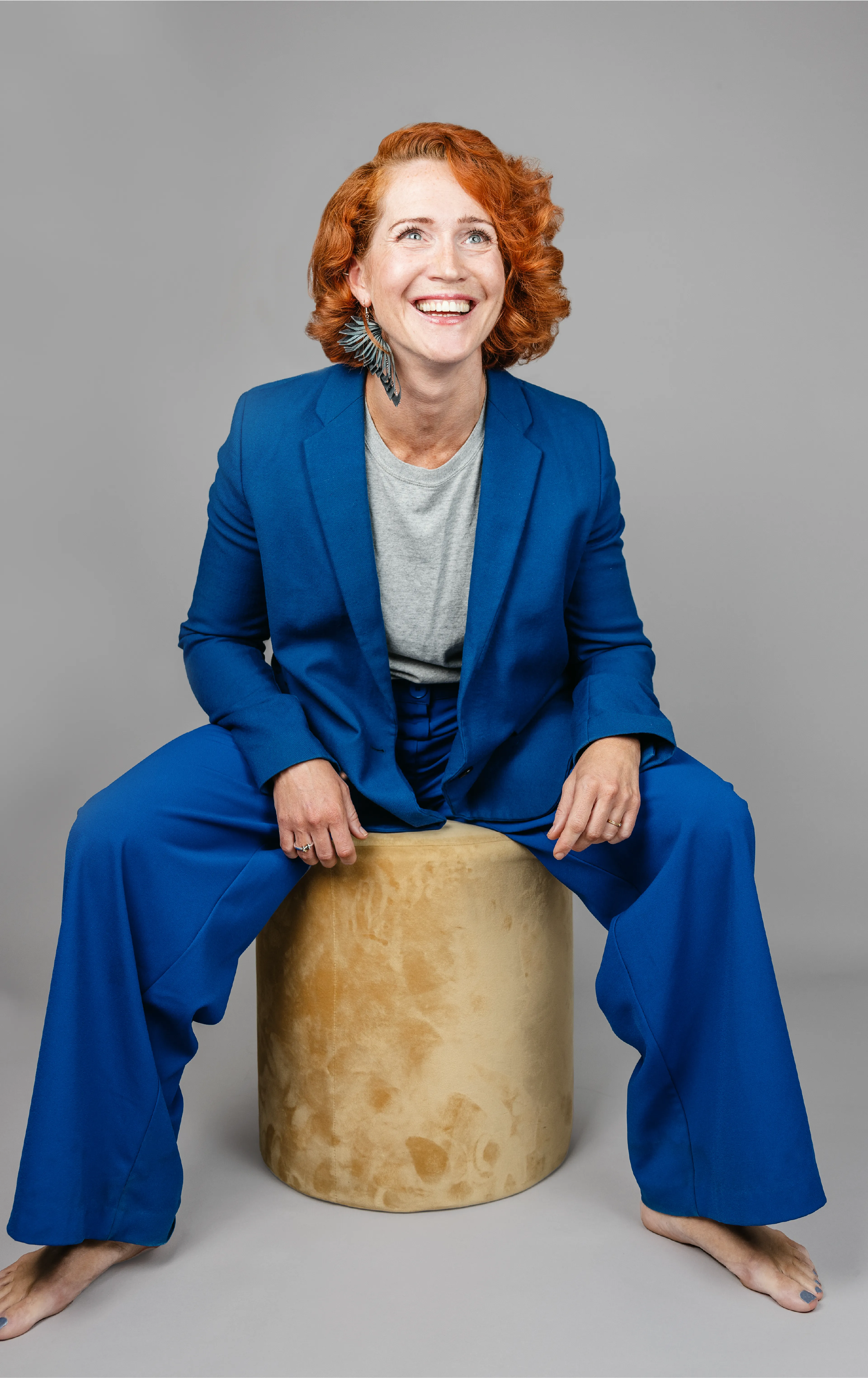 Woman with red hair in a blue suit sitting on a stool