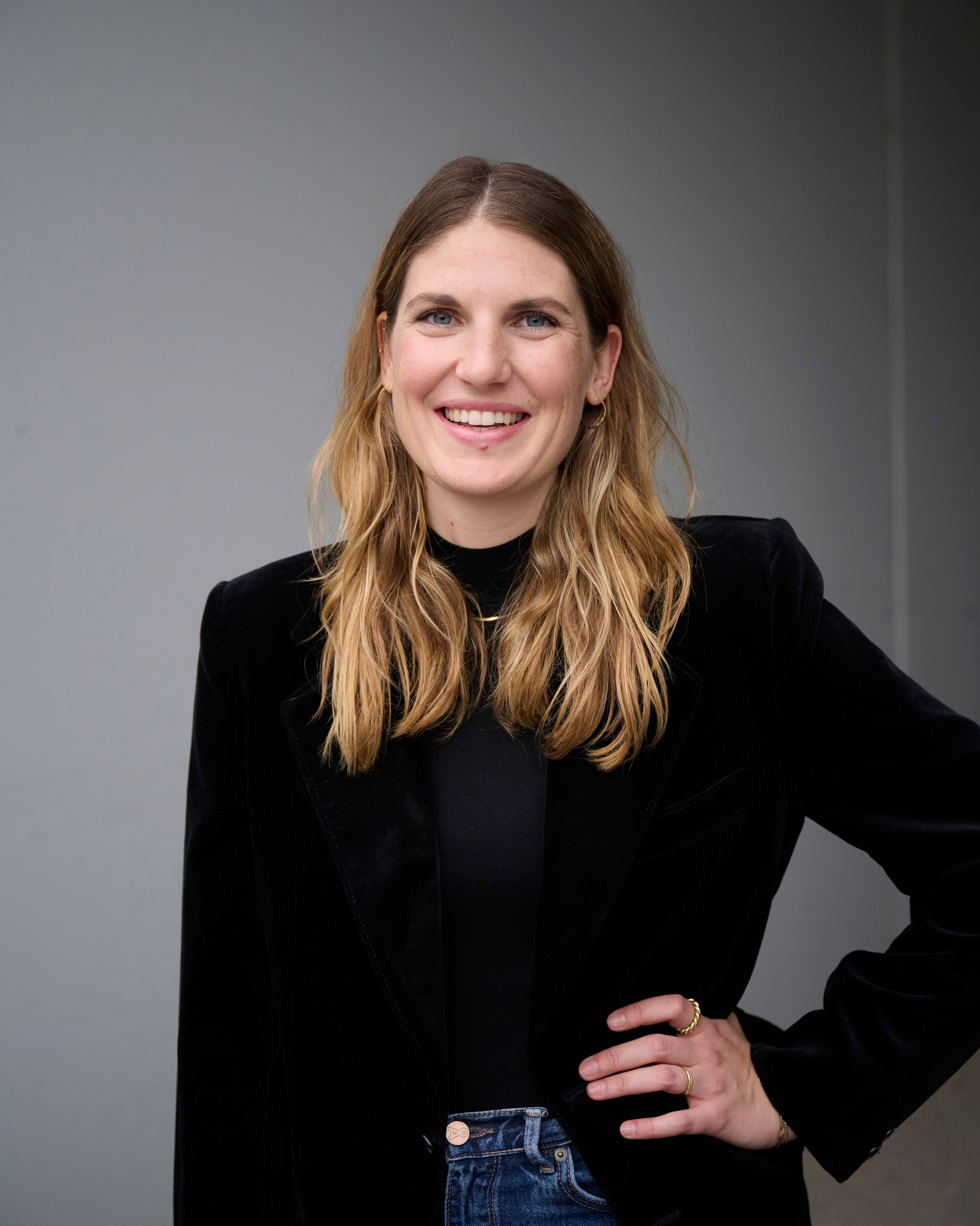 Smiling woman with a black shirt, standing with a hand on her hip.