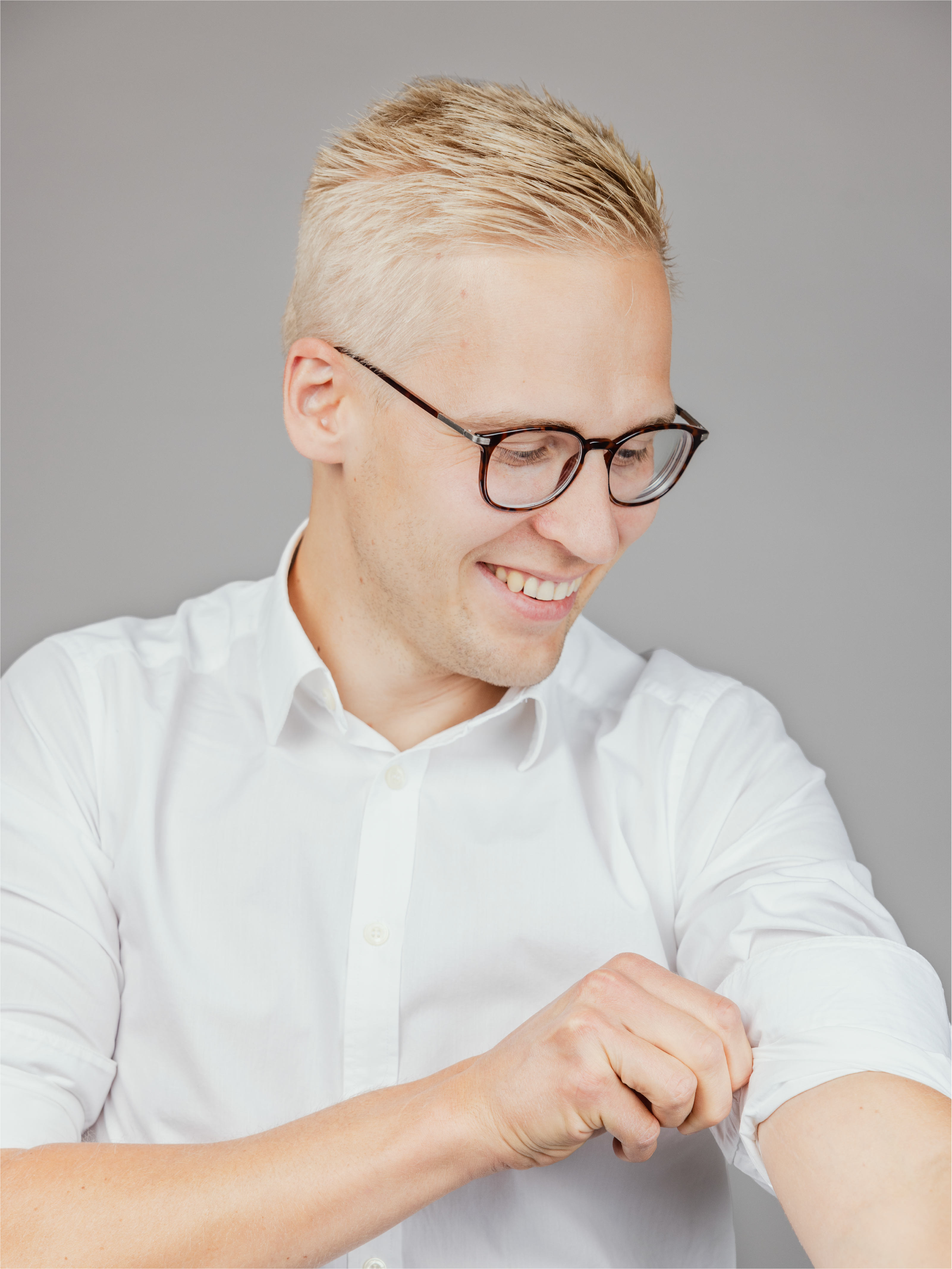 A man with glasses, rolling up the sleeve of his shirt